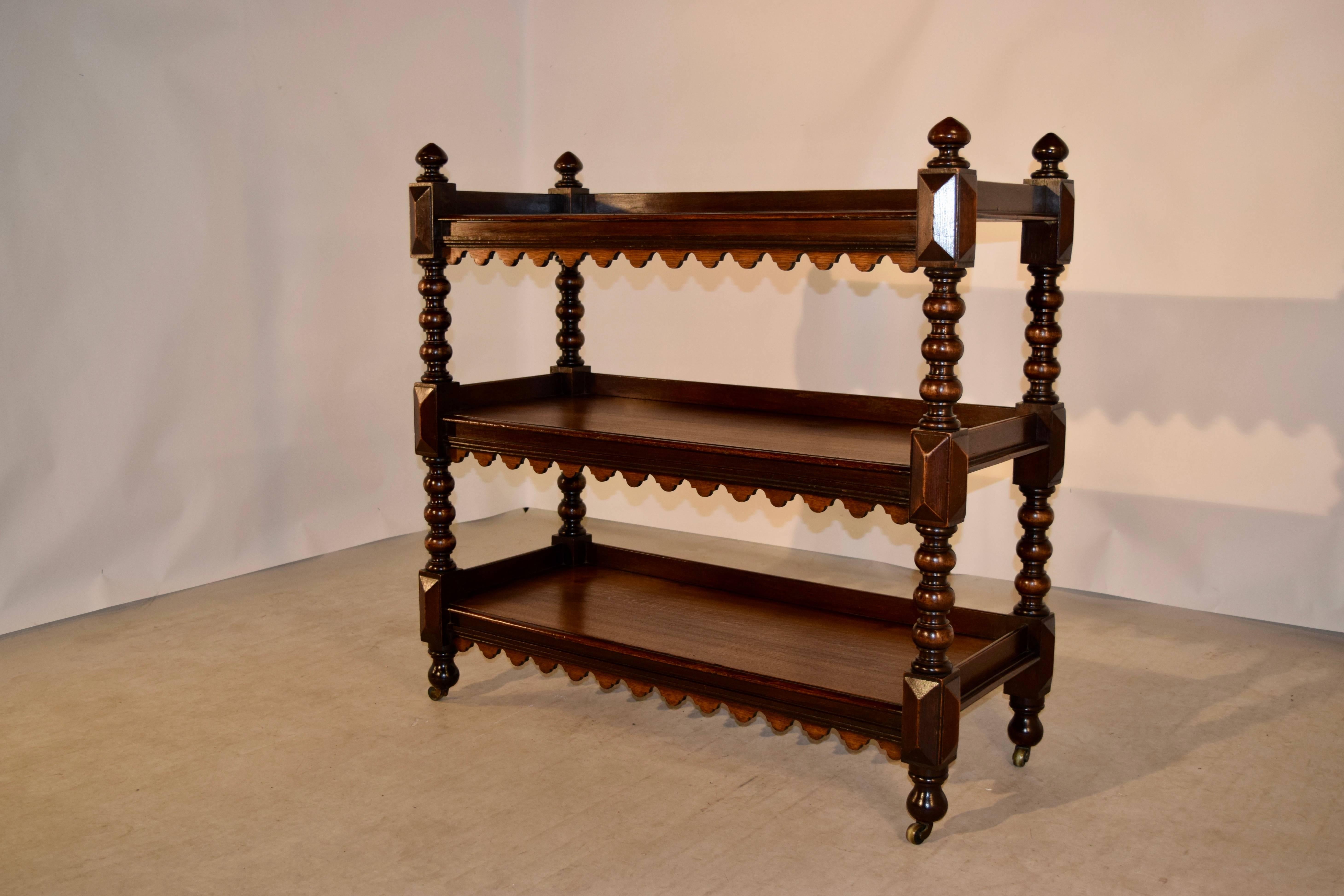 19th century oak buffet with three shelves from England. The top is decorated with finials, following down to three shelves, all with scalloped aprons and hand-turned shelf supports. Raised on hand-turned feet and casters.