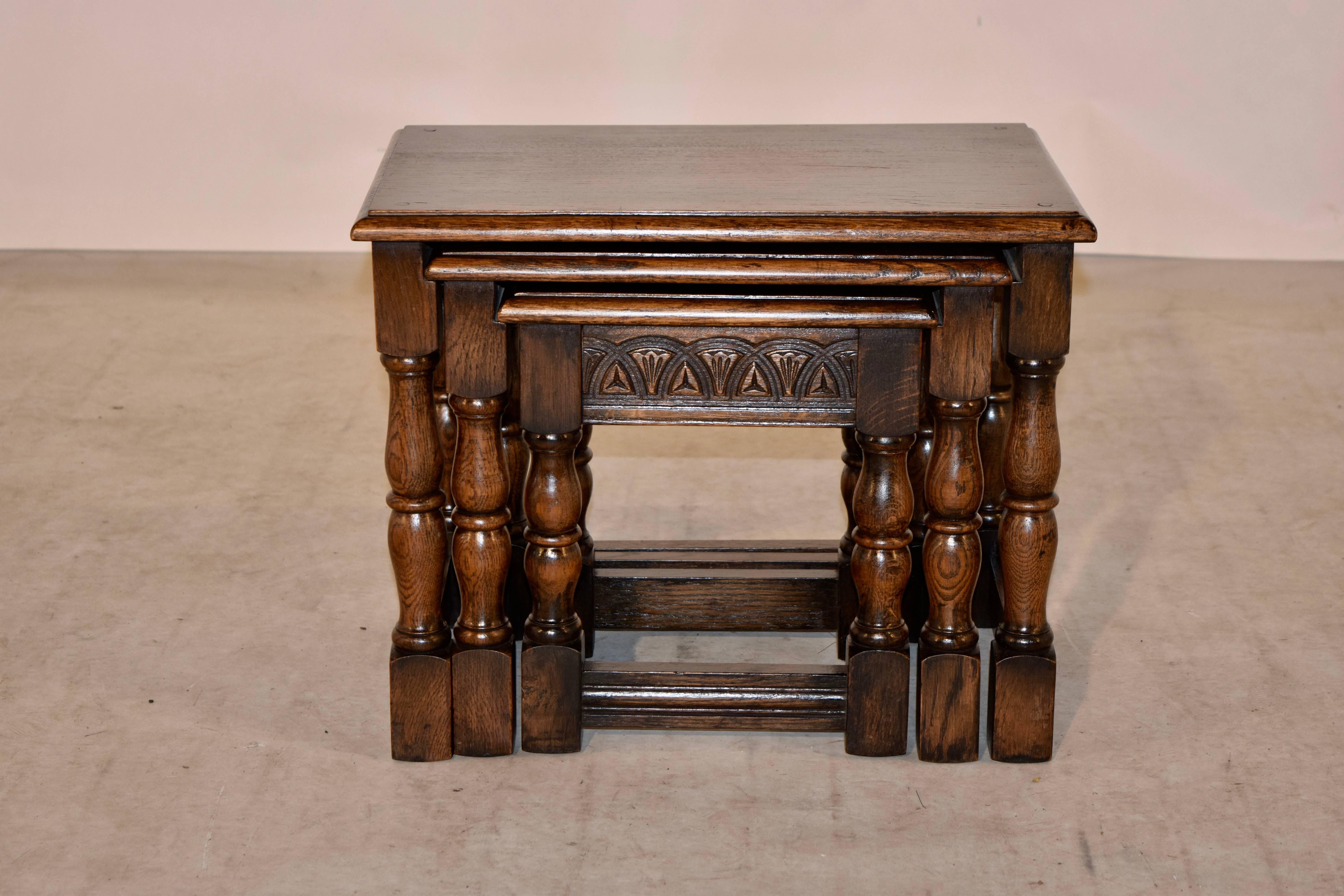 Nest of three oak tables with beveled edges around the tops, following down to hand-carved decorated aprons and supported on hand-turned legs, joined by reeded stretchers, circa 1900. The small table measures 12 x 9.63 x 13.5, and the medium table