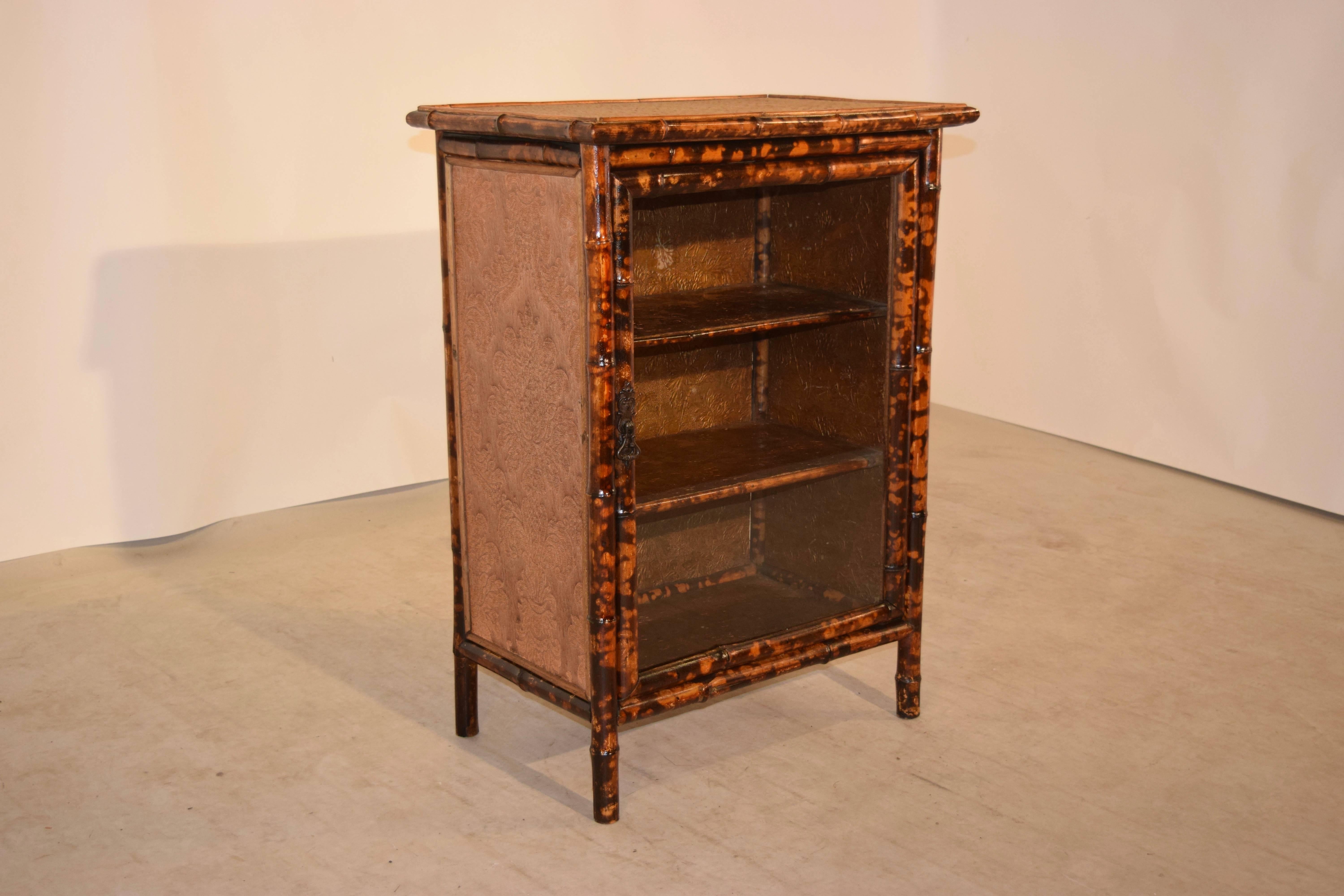 19th century bamboo bookcase from France with a rush covered top and fabric covered sides. There is a single glass door in the front, which opens to reveal three shelves, which are all covered in hand painted wallpaper, which gives it a fabulous