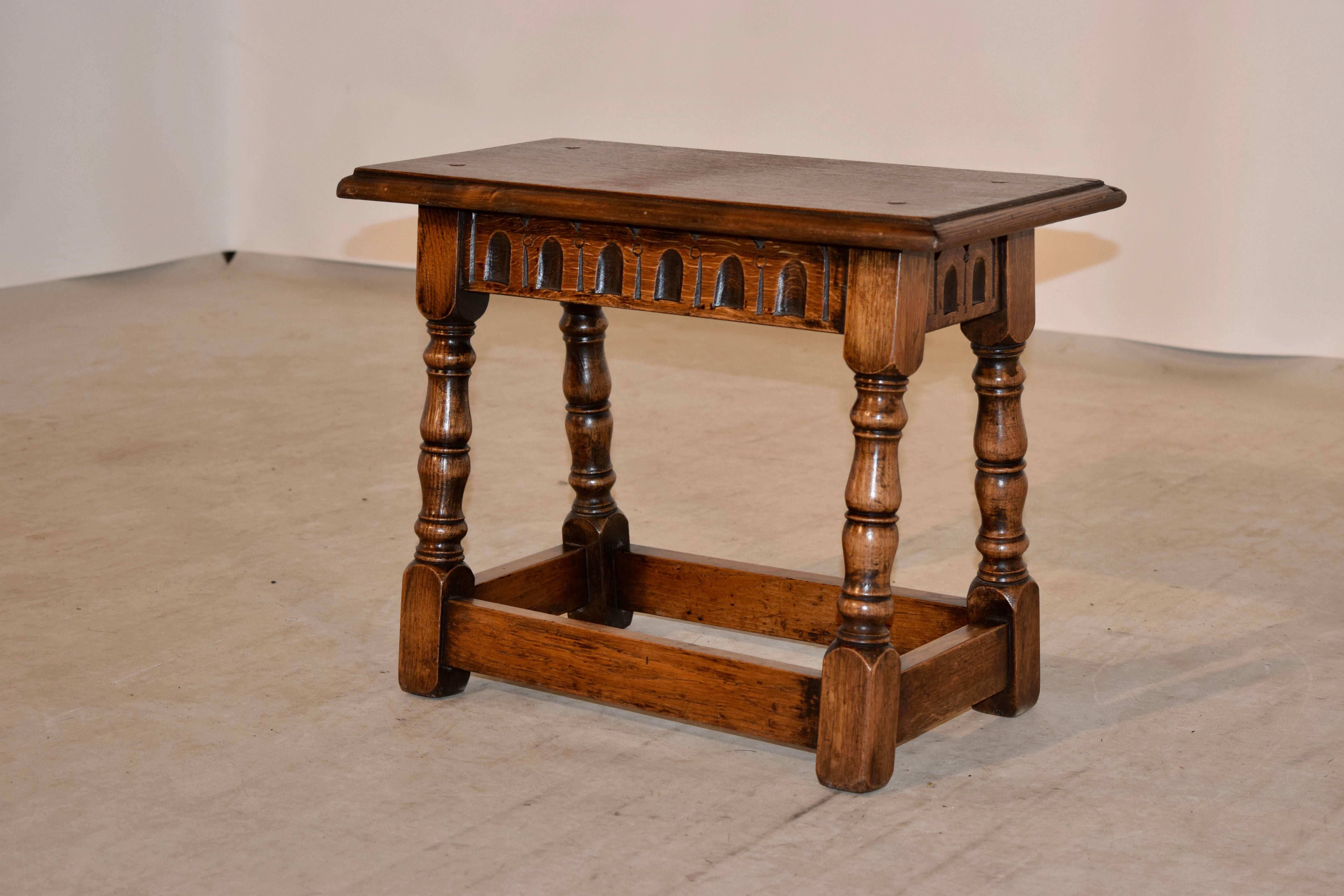 English oak joint stool with a beveled top following down to a fluted apron and hand turned splayed legs joined by stretchers. Hand pegged construction.