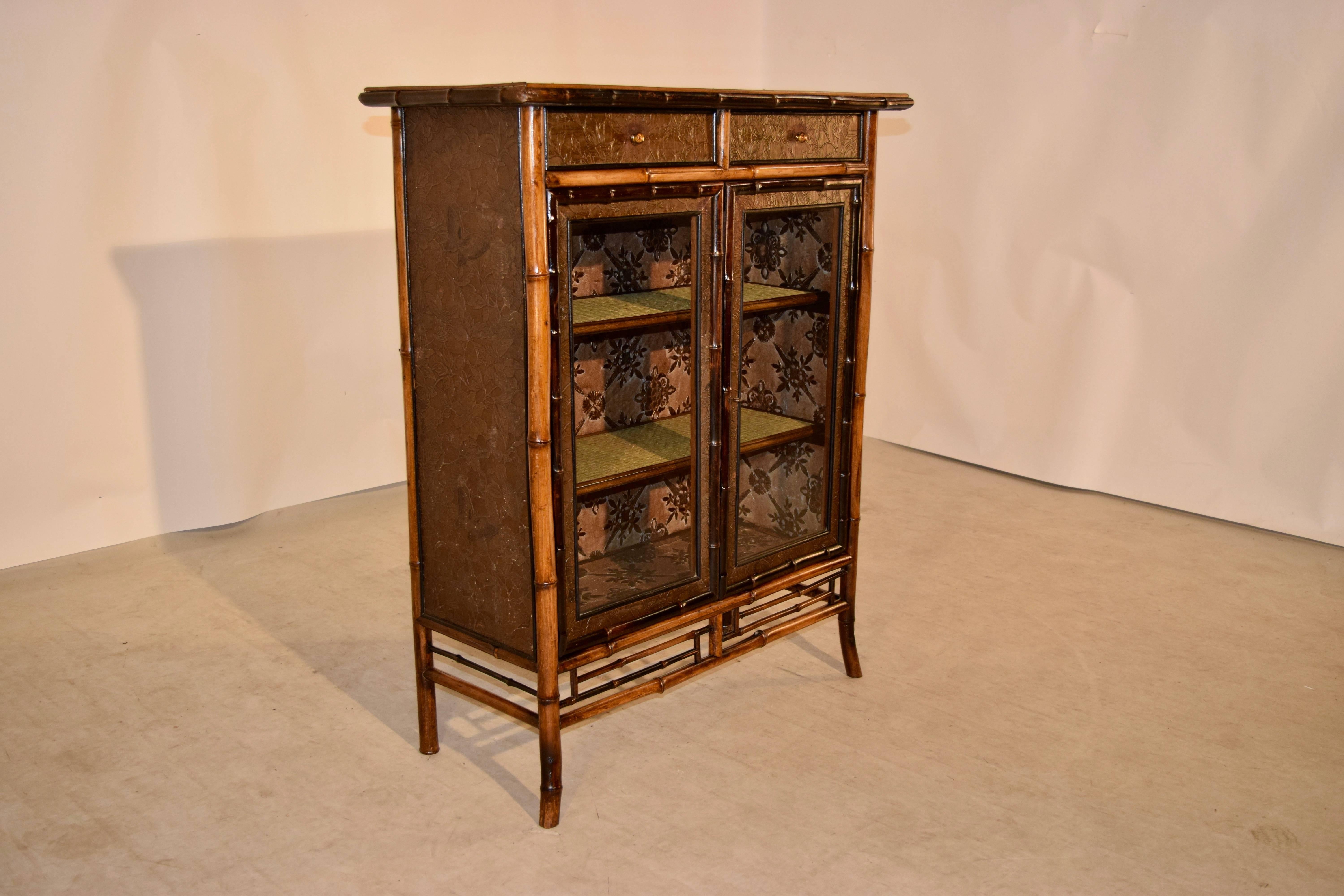 19th century French bamboo bookcase with a rush top and shelves. There are two drawers. The exterior and interior are covered in hand finished embossed wallpaper. The doors are framed glass. There is bamboo fretwork at the bottom of the case and it