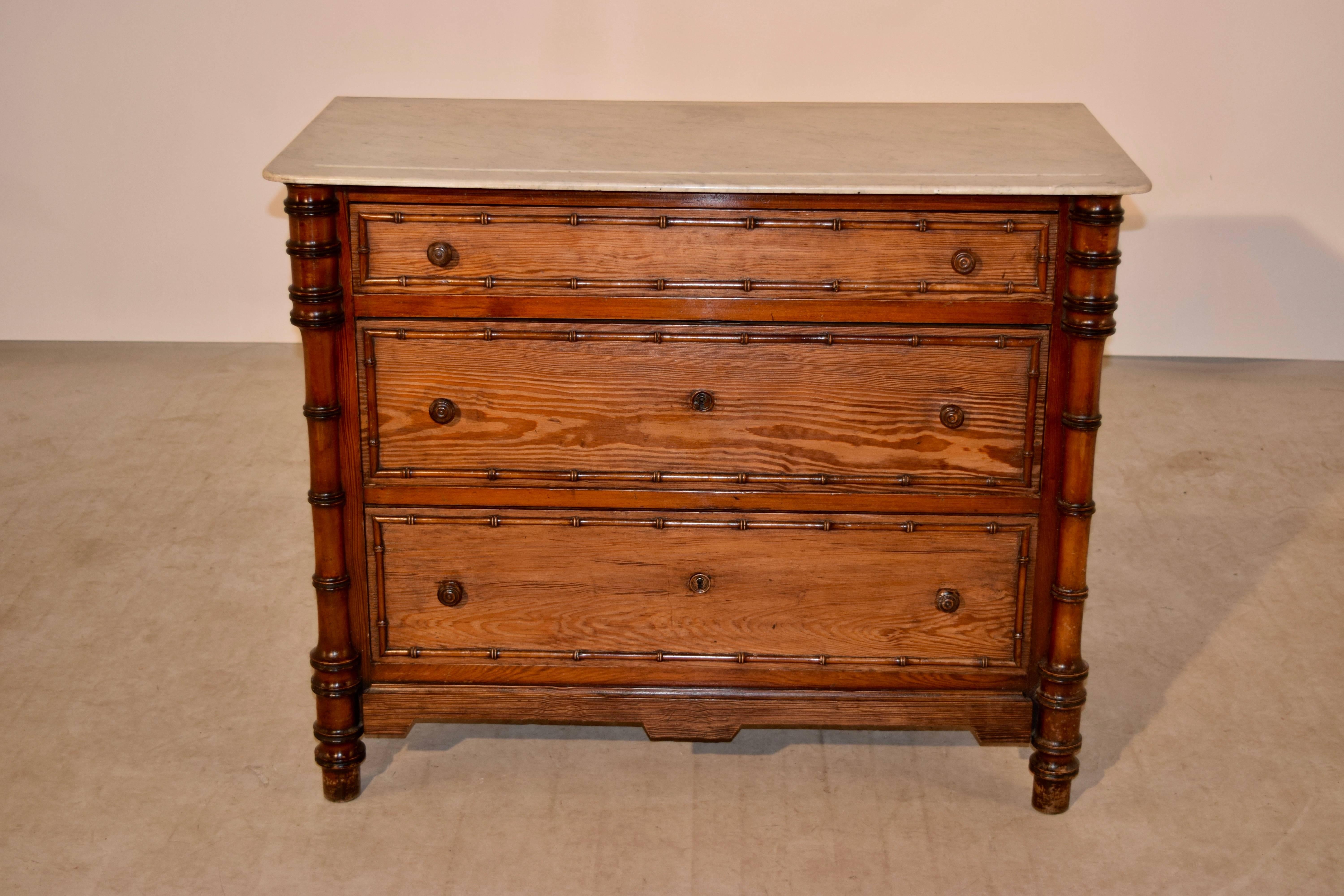19th century pitch pine chest from France with a marble top, following down to paneled sides and three drawers in the front, with faux bamboo carved molding surrounding the drawers, and flanked with faux bamboo turned columns. The apron is shaped on