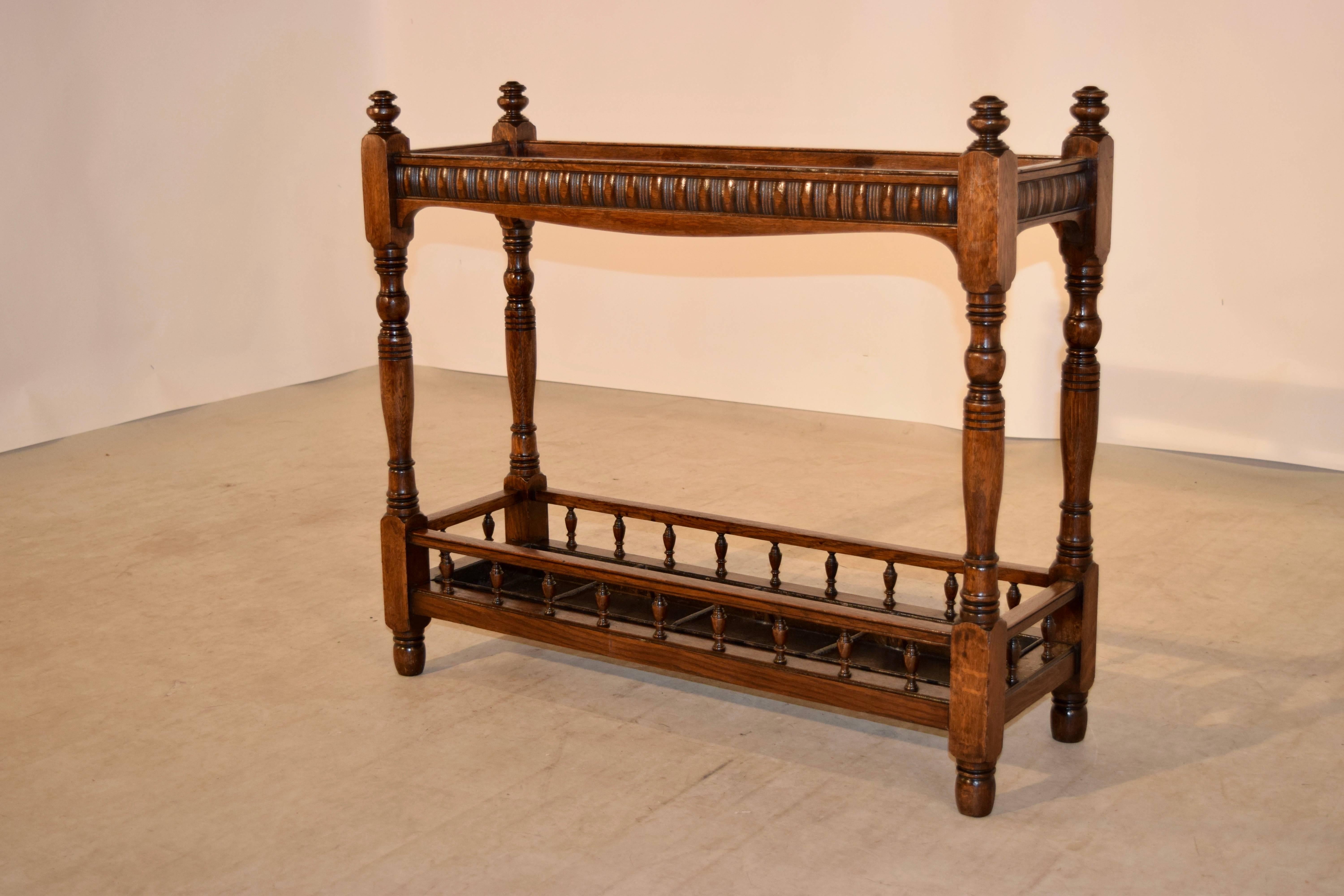 19th century English oak umbrella and cane stand with finials, following down to hand-turned legs, joined at the top by hand-carved decorated rails and at the bottom by simple rails with hand-turned spindles. It retains the original painted metal