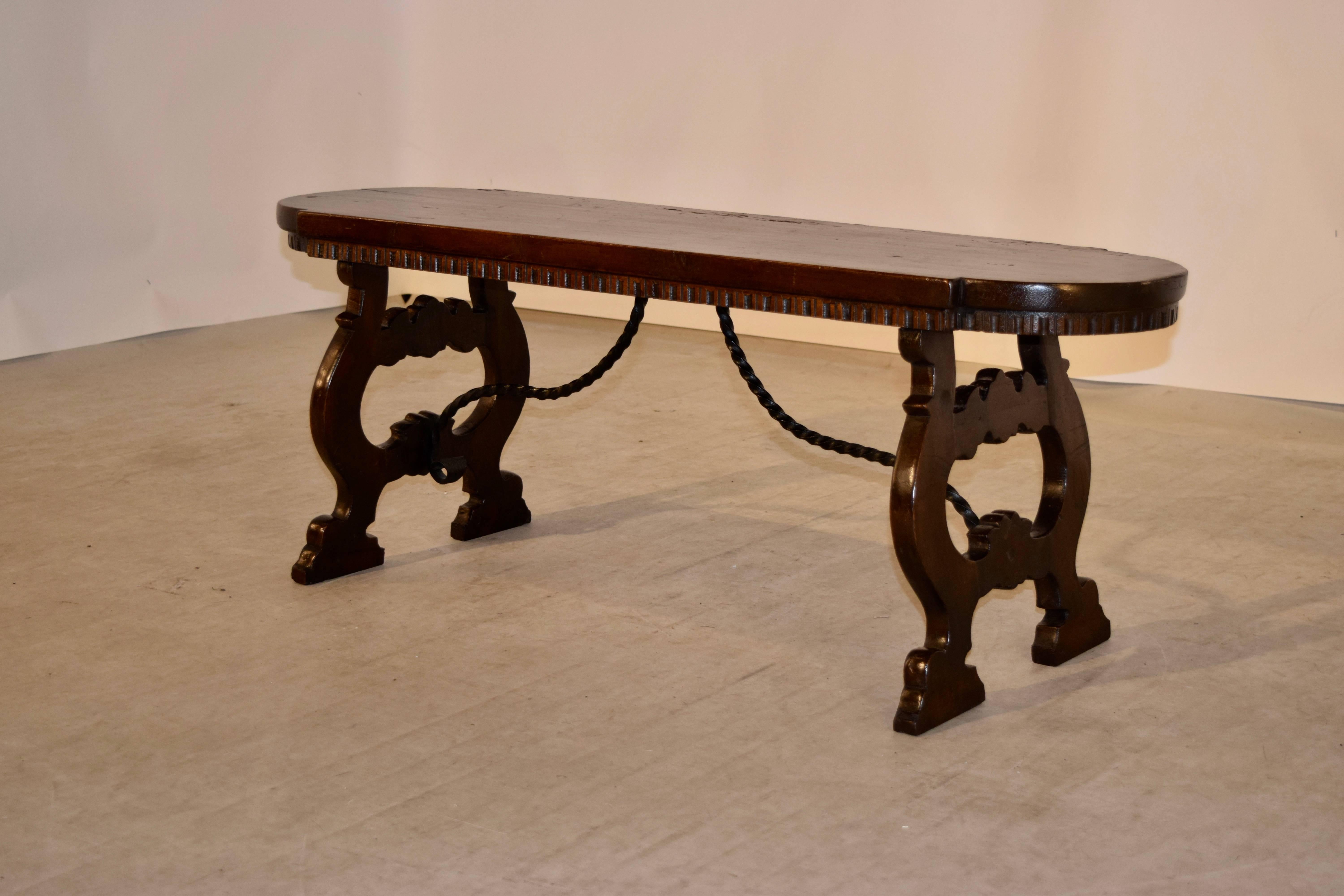 1920's Continental walnut bench in the Spanish Revival style.  The top is shaped and has wear on the edges from age and use.  The apron underneath the top is carved decorated and is supported on lyre shaped legs, joined to the bench by iron