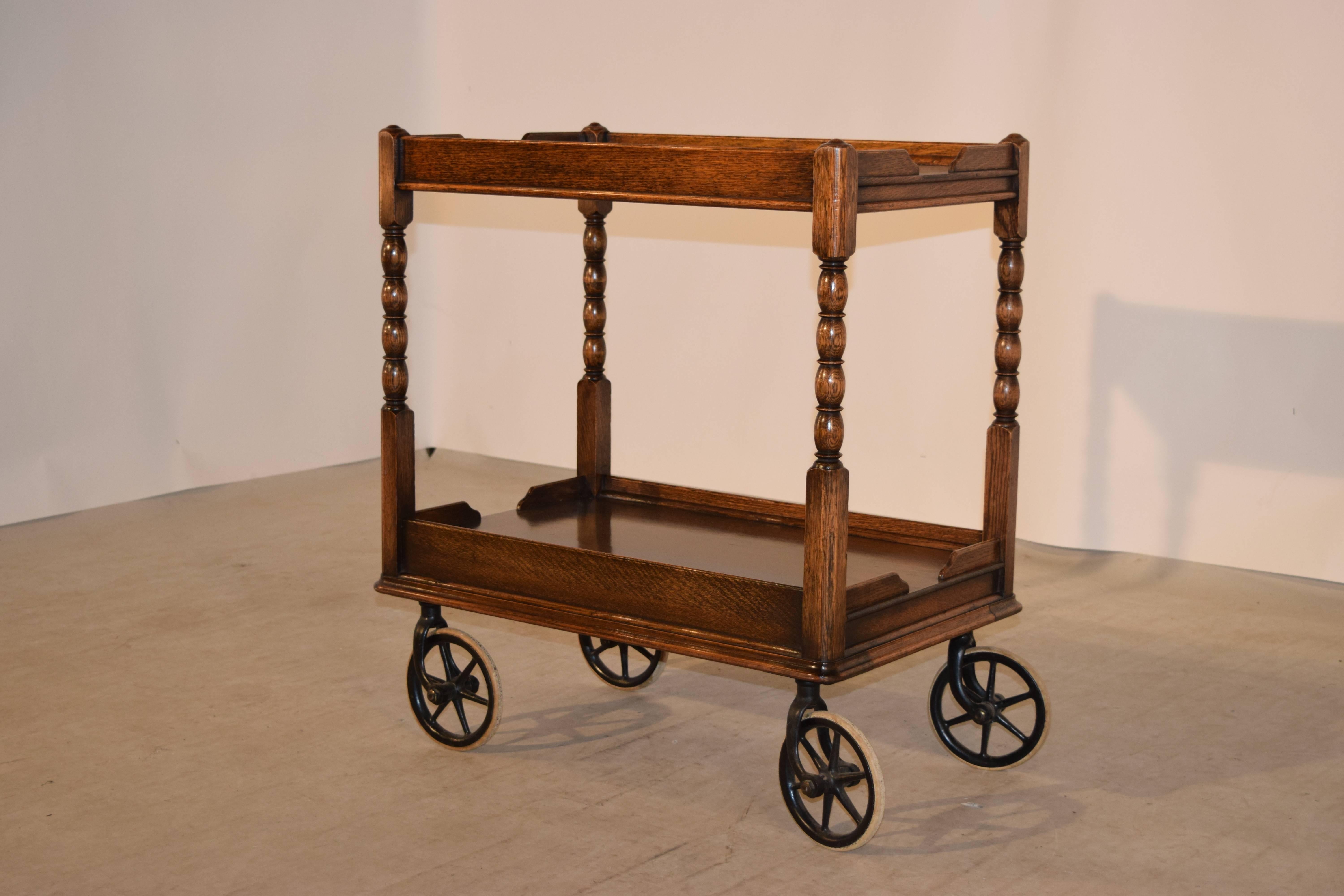 19th century English oak drinks cart with a molded gallery around the top and lower shelf, separated by hand turned bob and stop shelf supports. It is raised on the original wheels, which are unusually large, which gives it a whimsical look.