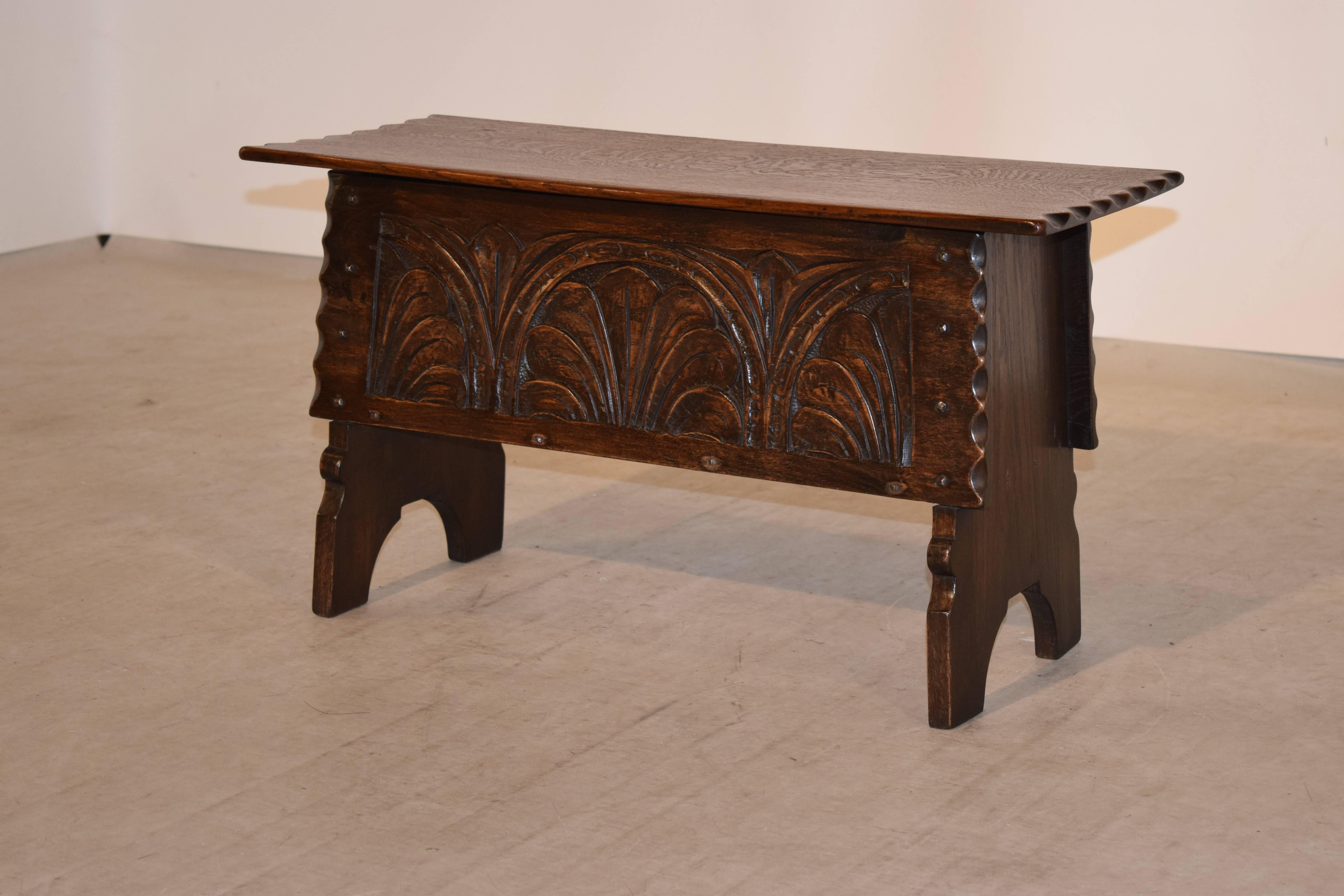 19th century oak bench with a lift top from England. The top is a single board with a pie crust edge, following down to a carved panel on the front, also with a pie crust edge. It has simple legs that are joined to the front and back with hand made