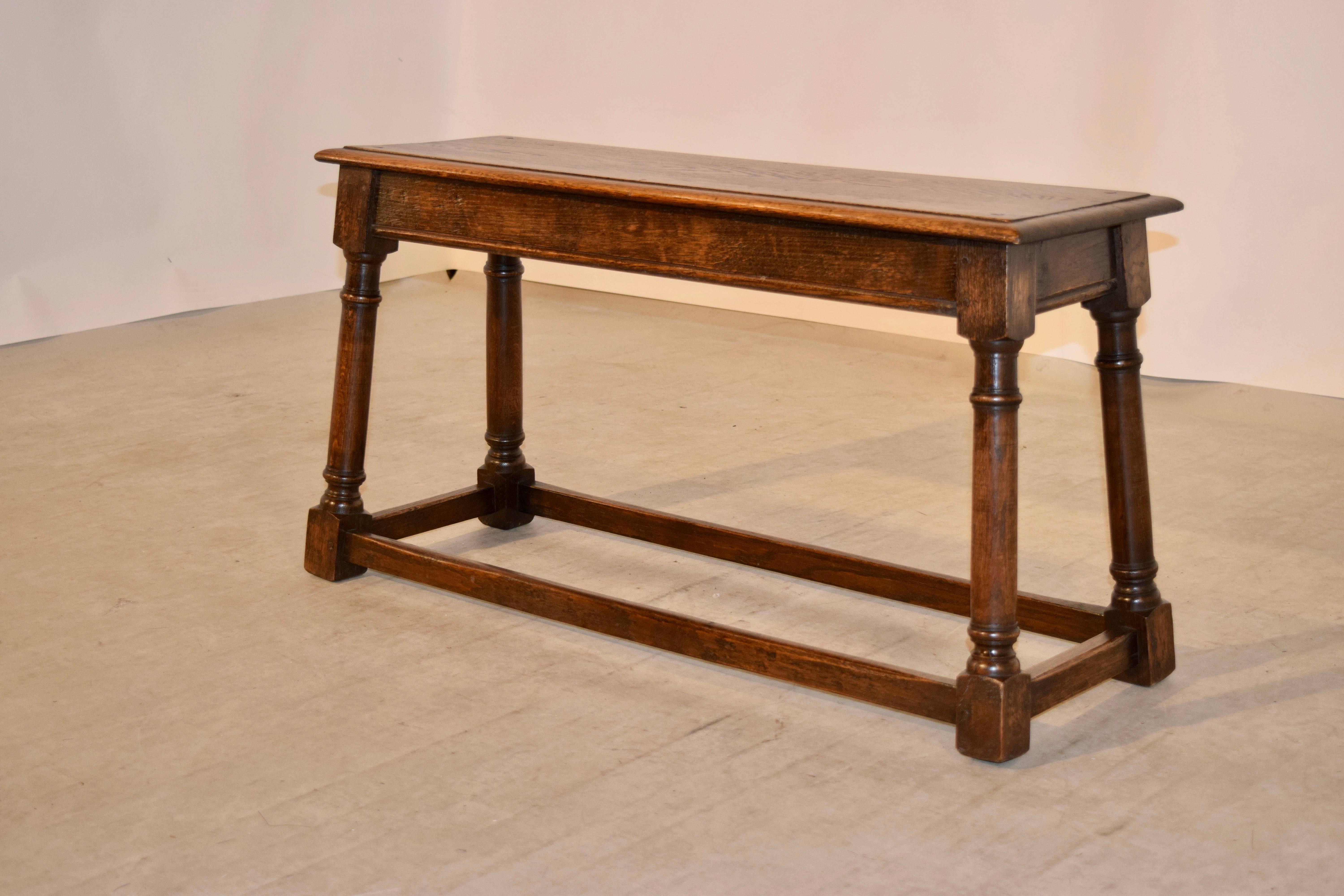 19th Century oak bench from England with a beveled edge around the top, following down to a simple apron and supported on hand turned splayed legs joined by stretchers.  The seat measures 36 w x 11.75 d.