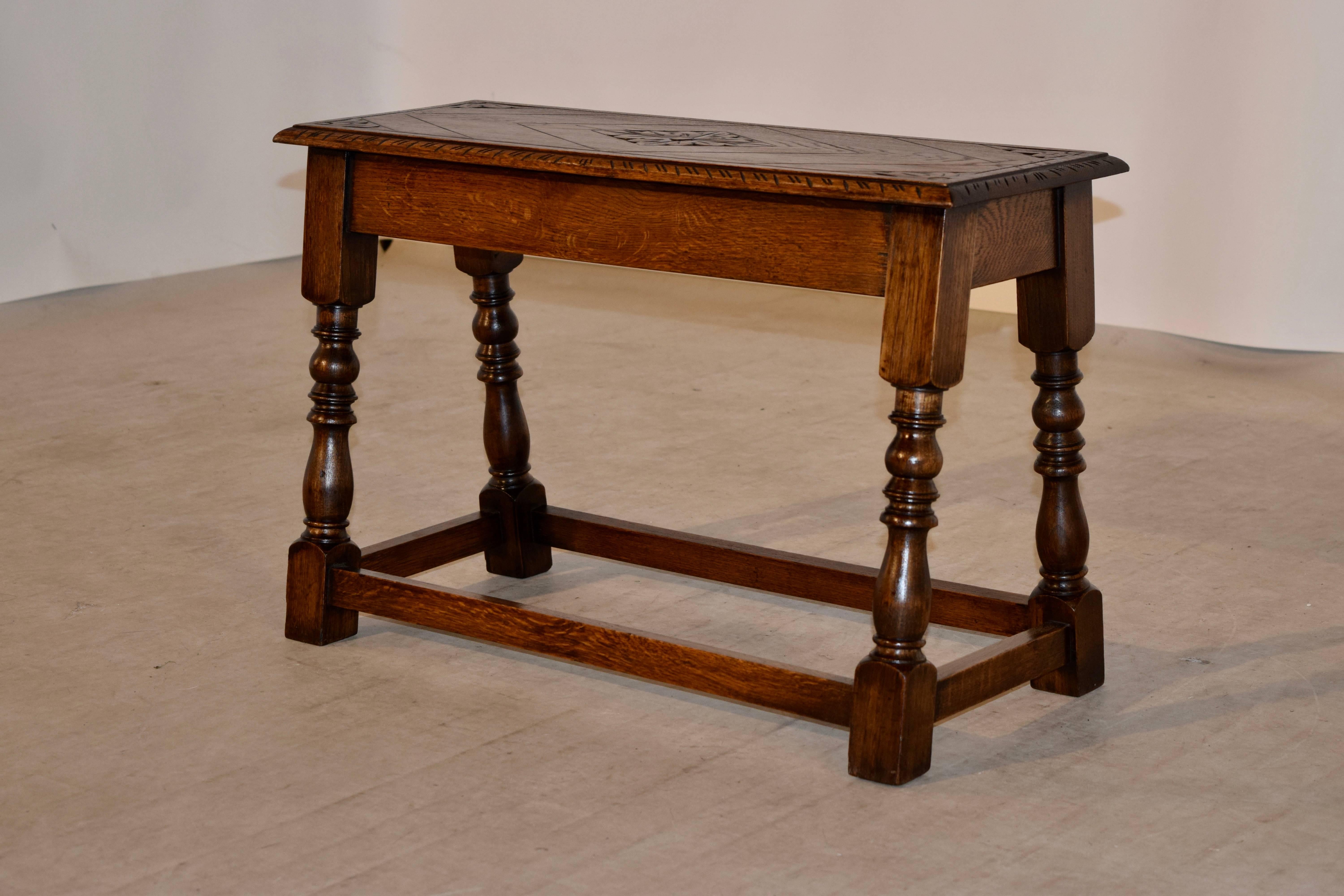 Small English oak bench with a carved decorated top and a bevelled and carved edge. This follows down to a simple apron and splayed legs, joined by simple stretchers.