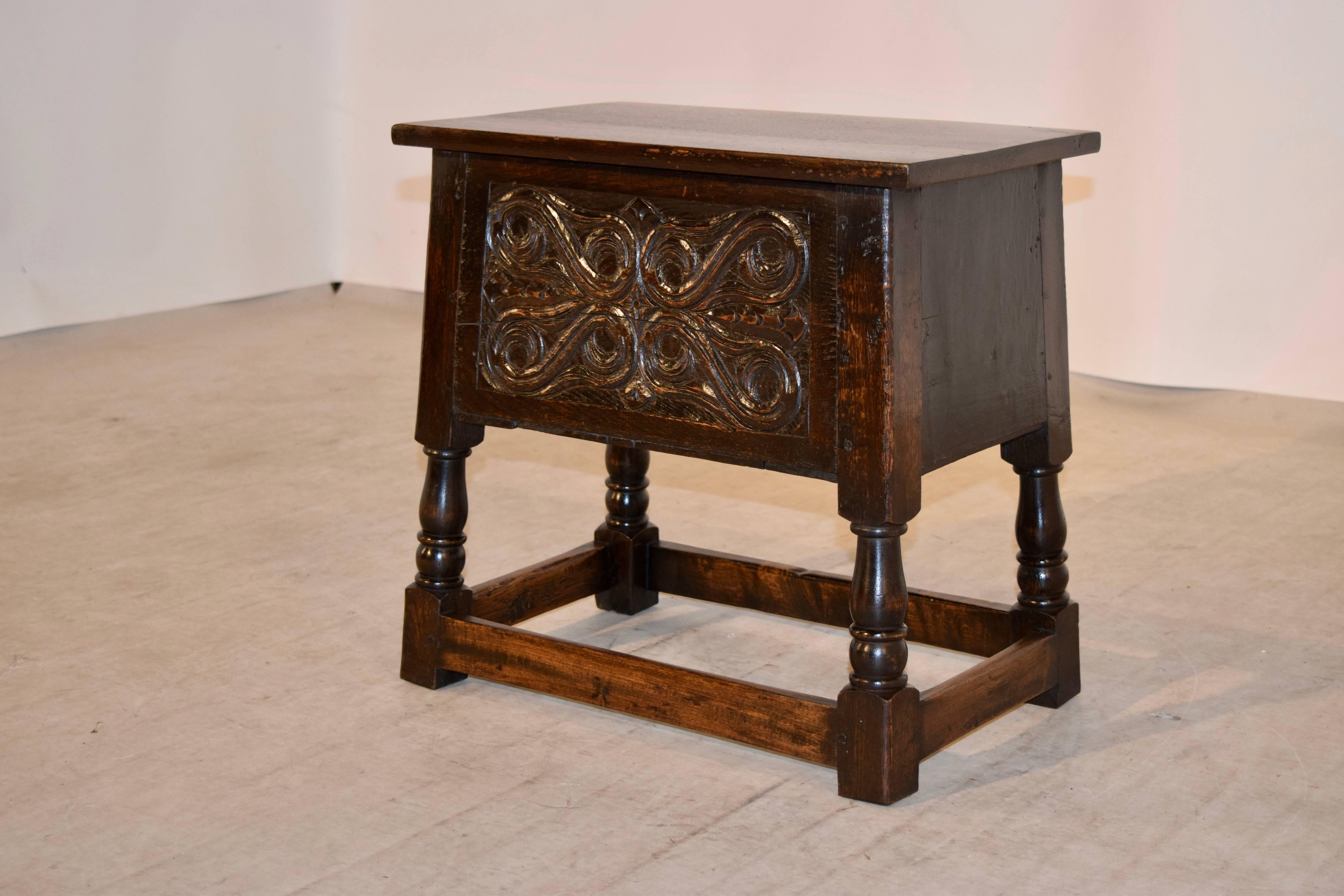 Late 19th century lift top oak stool from England. The top lifts to reveal a nice storage compartment. The front panel is hand-carved decorated, and the piece is supported on sturdy hand turned splayed legs joined by stretchers.