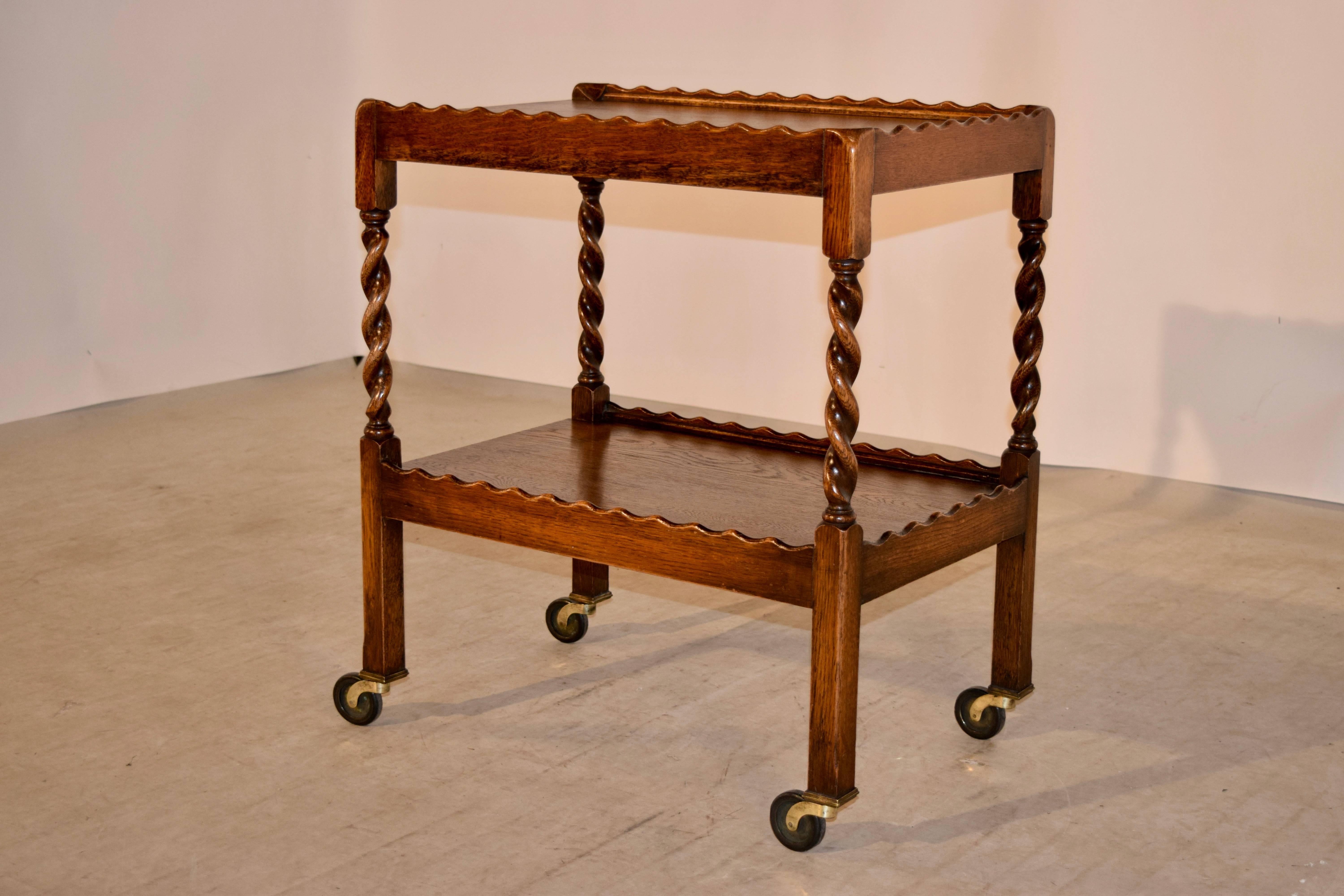 19th century English oak drinks cart with a wonderfully scalloped galleries on both shelves, separated by hand turned barley twist legs, which end in straight legs on original casters.