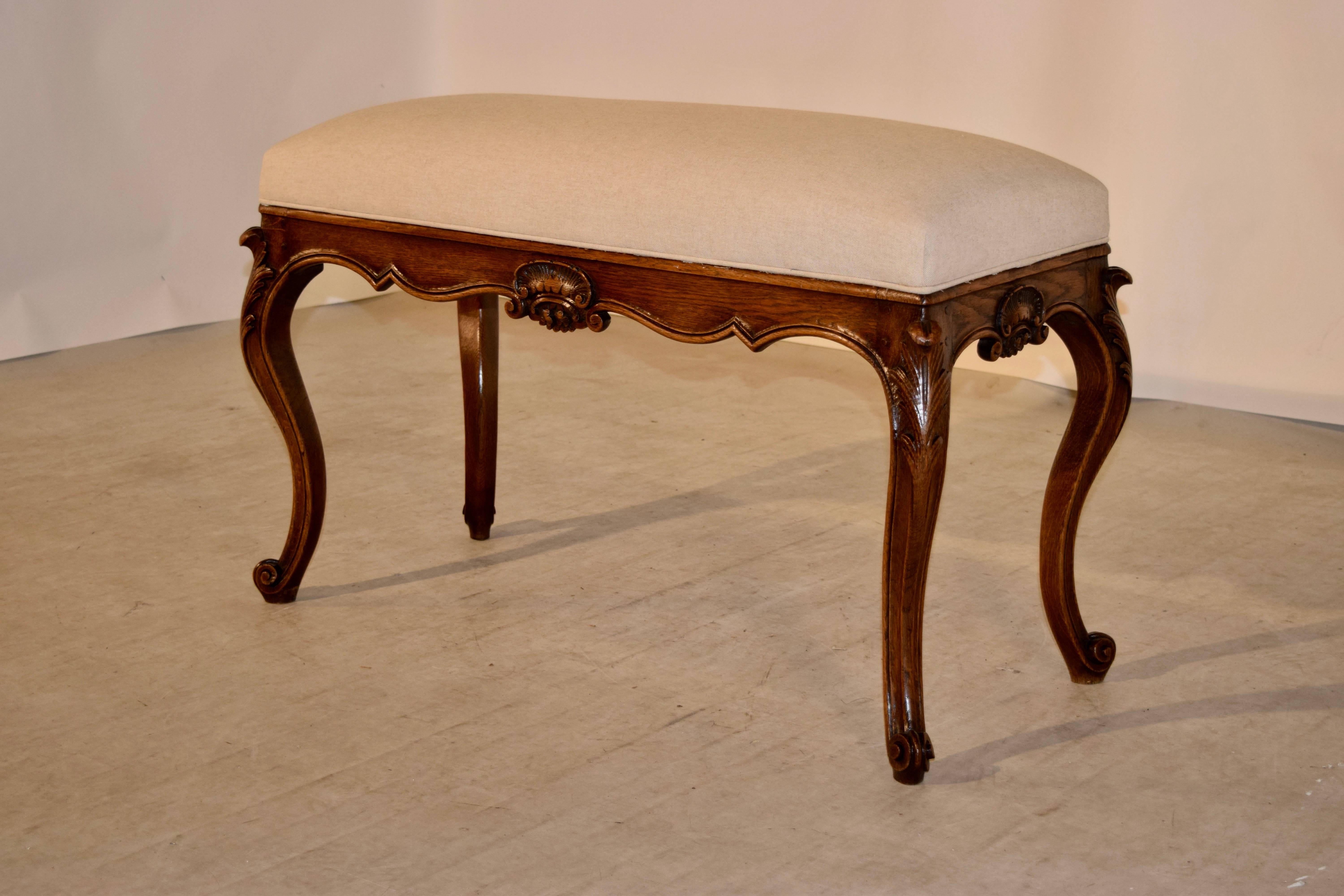 19th century French bench with a newly upholstered top in linen. The frame is hand carved from oak and has a scalloped apron, which has hand-carved shell embellishments and wonderful cabriole legs ending in scroll feet.