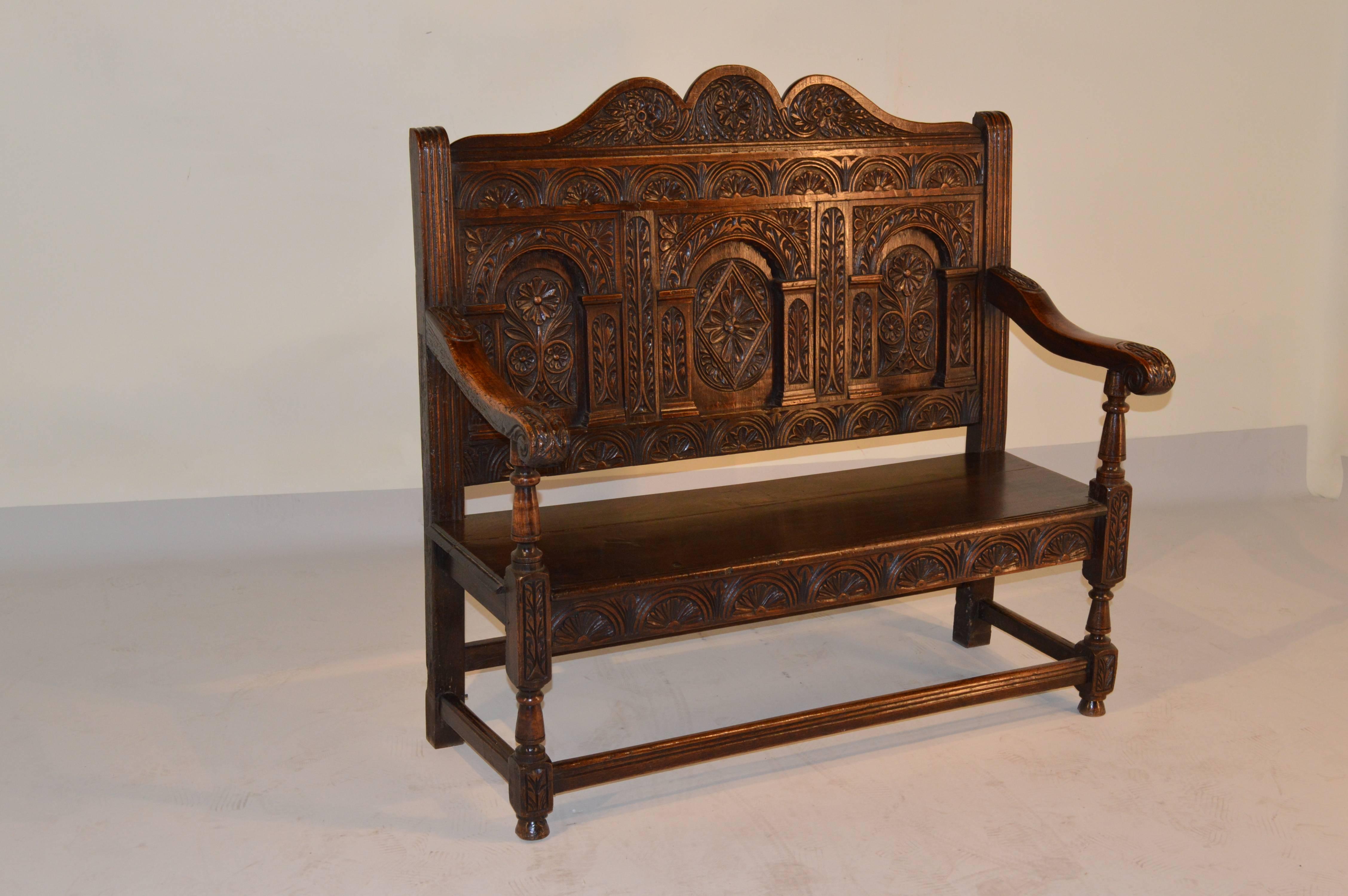 Early 19th century English oak carved settee.  The back is splendidly scalloped at the top following down to hand carved decorated raised panels with arched decoration.  The arms are scrolled and supported on hand turned supports.  The apron is