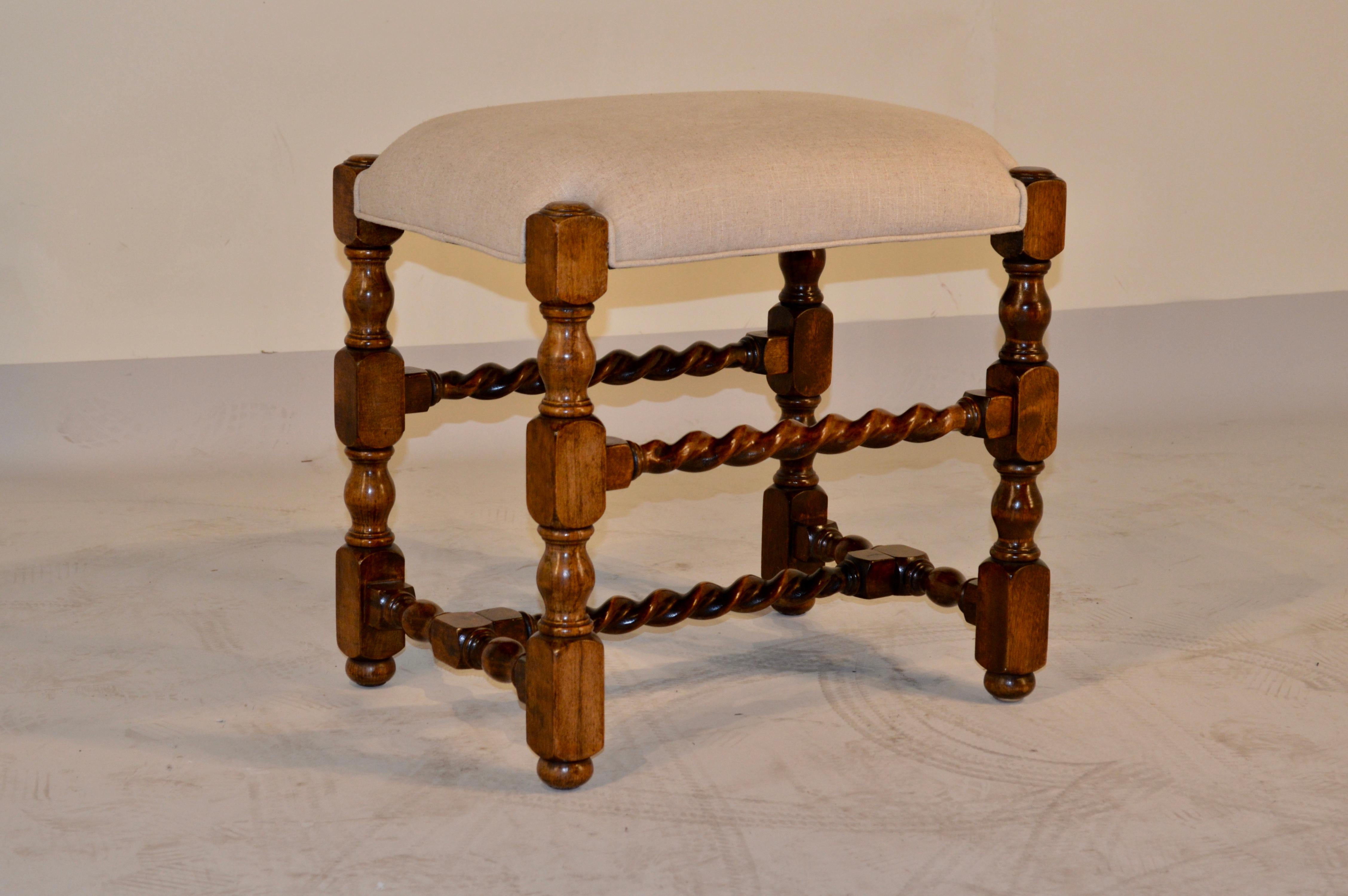 Late 19th century English oak turned stool with nicely hand turned legs and barley twist joining stretchers.  Raised on turned feet.  There is shrinkage in one leg.  The seat has been newly upholstered in linen and is finished with a single welt.