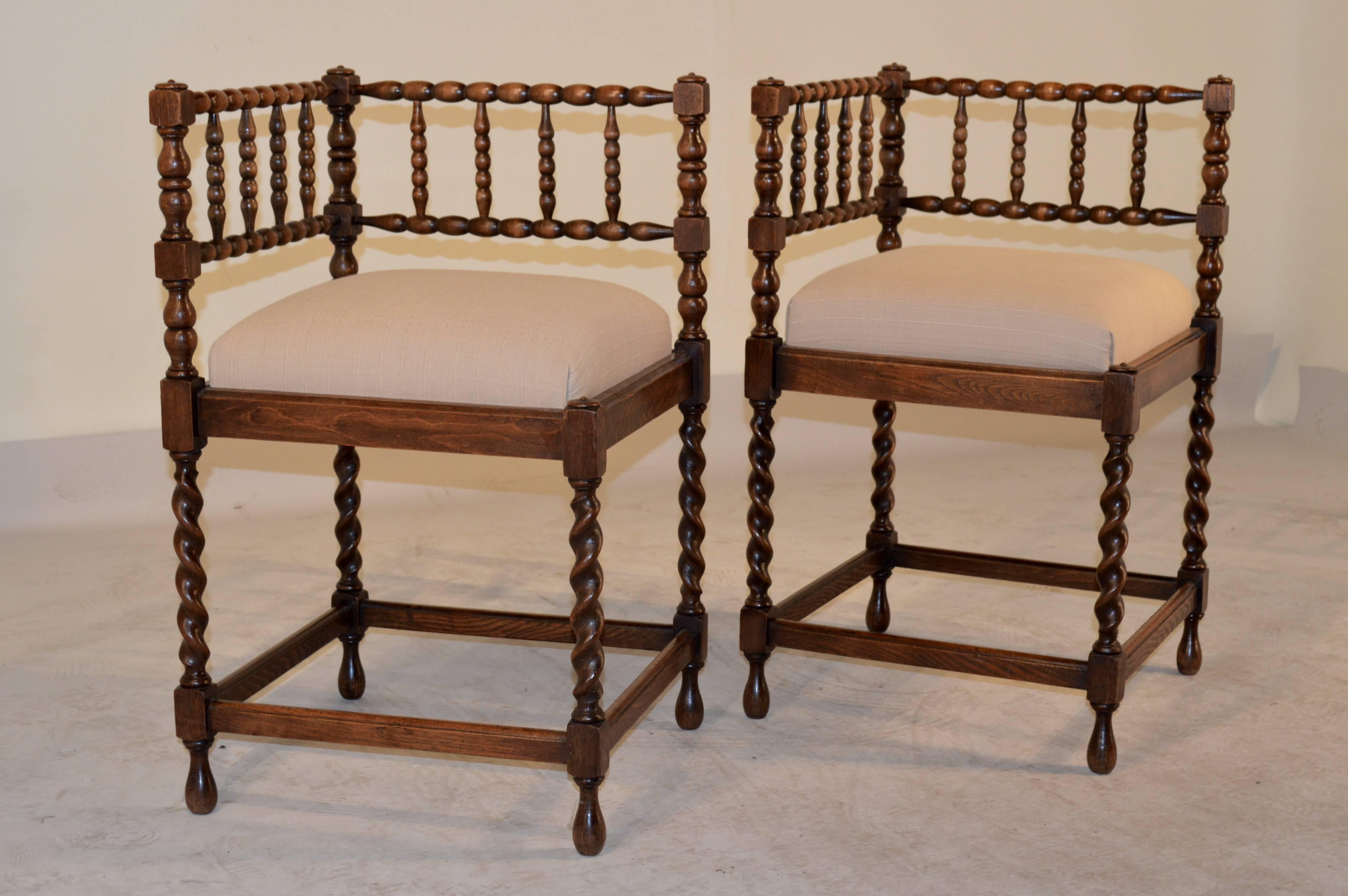 19th Century pair of French corner chairs made from oak.  The backs of the chairs are made up of spool spindles and rails, joined by hand turned pieces.  The legs are hand turned barley twist, and are joined by stretchers and raised on turned feet. 