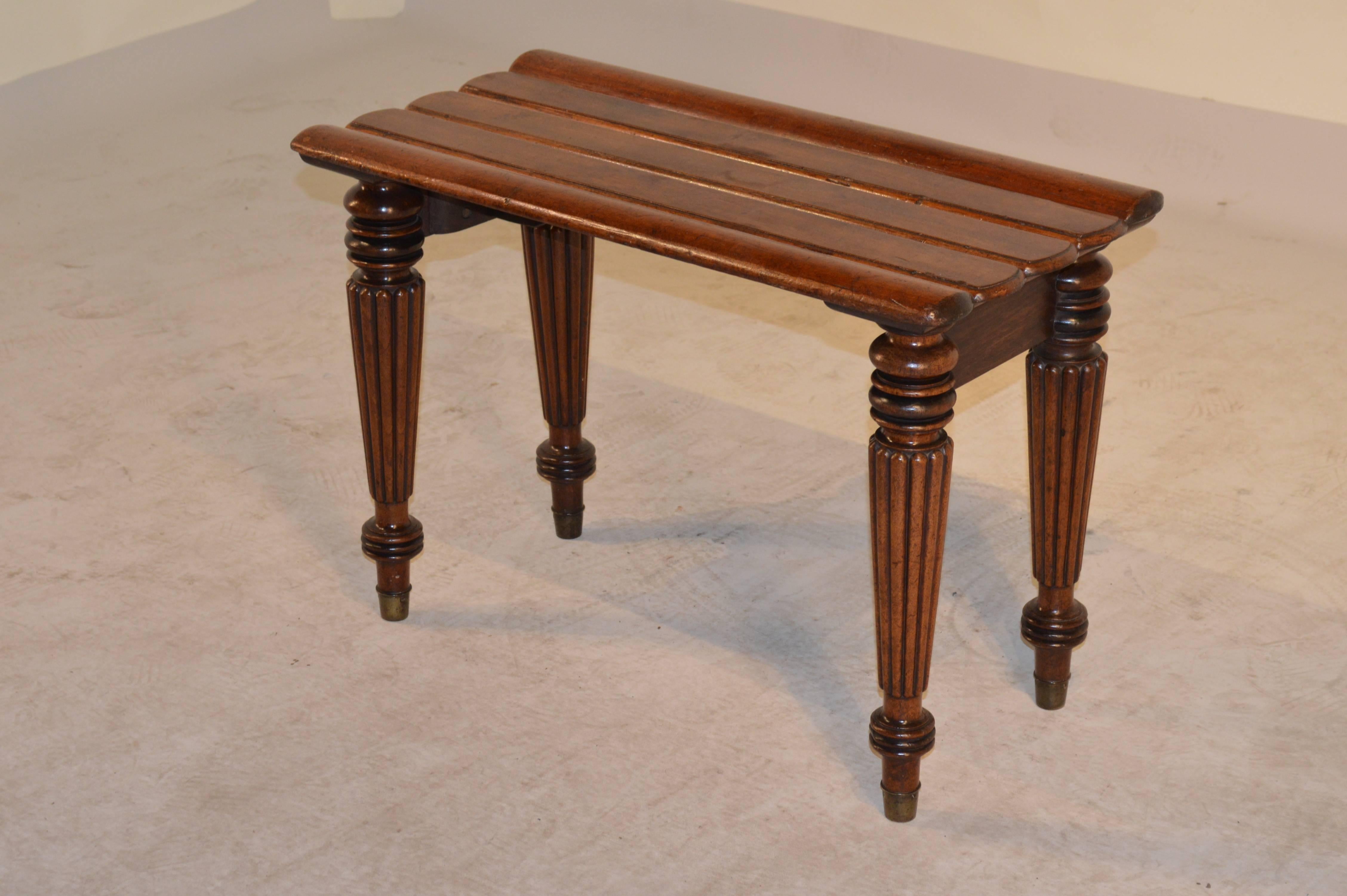19th Century English mahogany luggage stand with shaped slats on top and a simple apron following down to wonderfully reeded and turned legs and tapered feet with original brass caps.