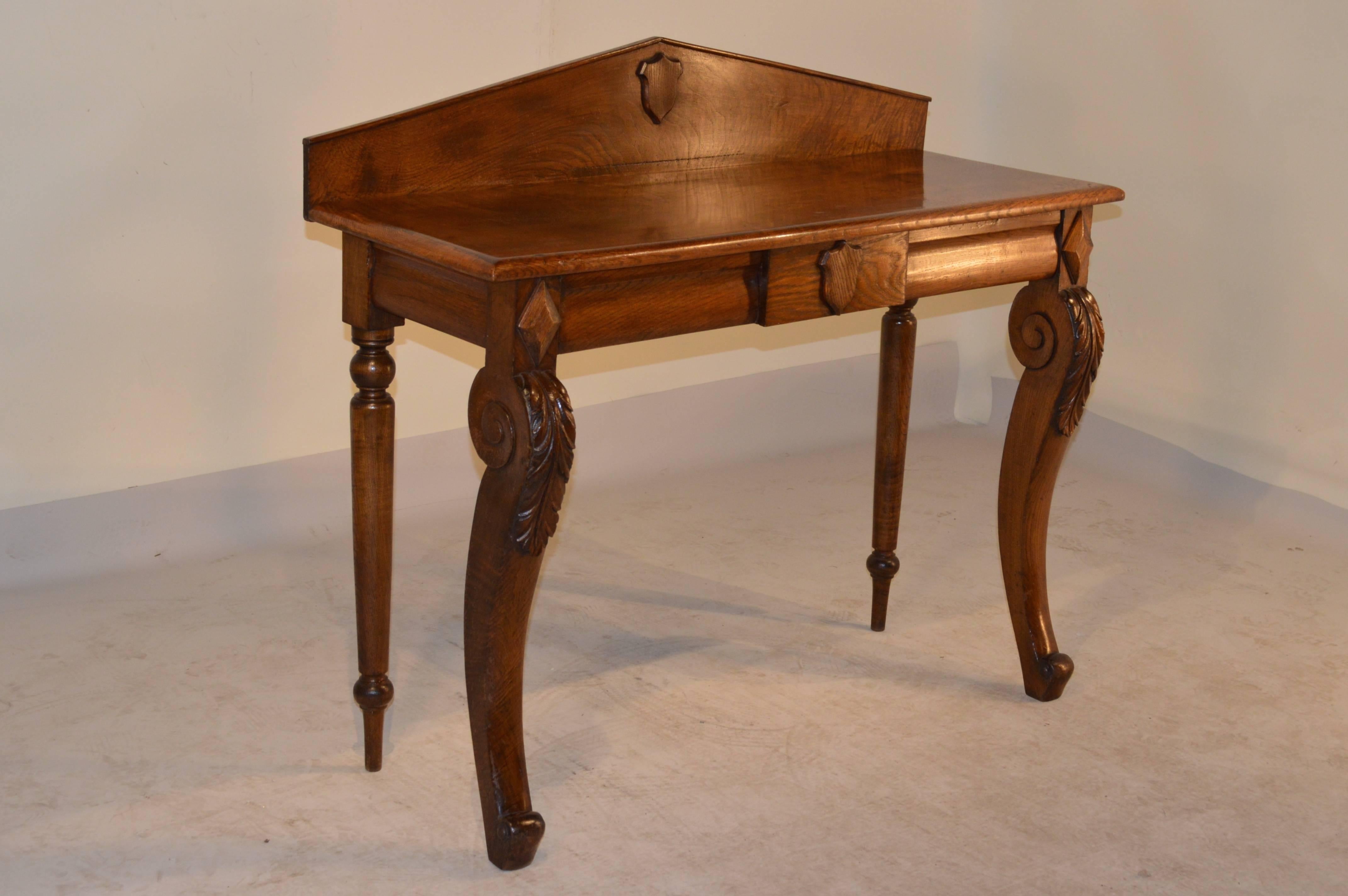 19th Century English console table made from oak with a peaked back splash which is decorated with a wooden shield.  The graining in the top is fantastic and follows dow to a simple apron with a single drawer, which also has a matching shield