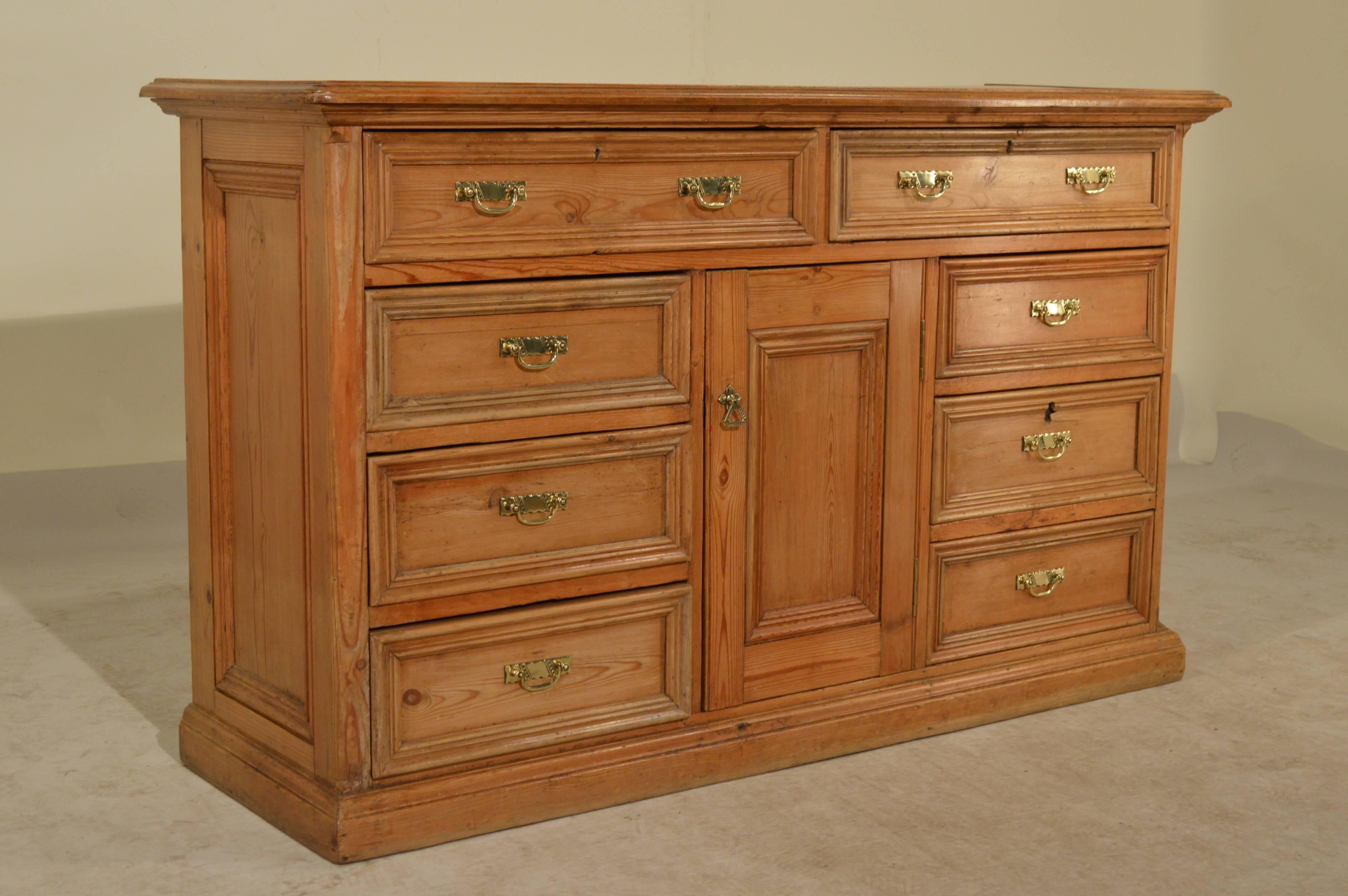 19th Century English dresser base made from pine with a beveled and molded edge around the top following down to raised paneled sides and two top drawers over a single door, flanked on each side by three drawers.  All of the drawers are wonderfully