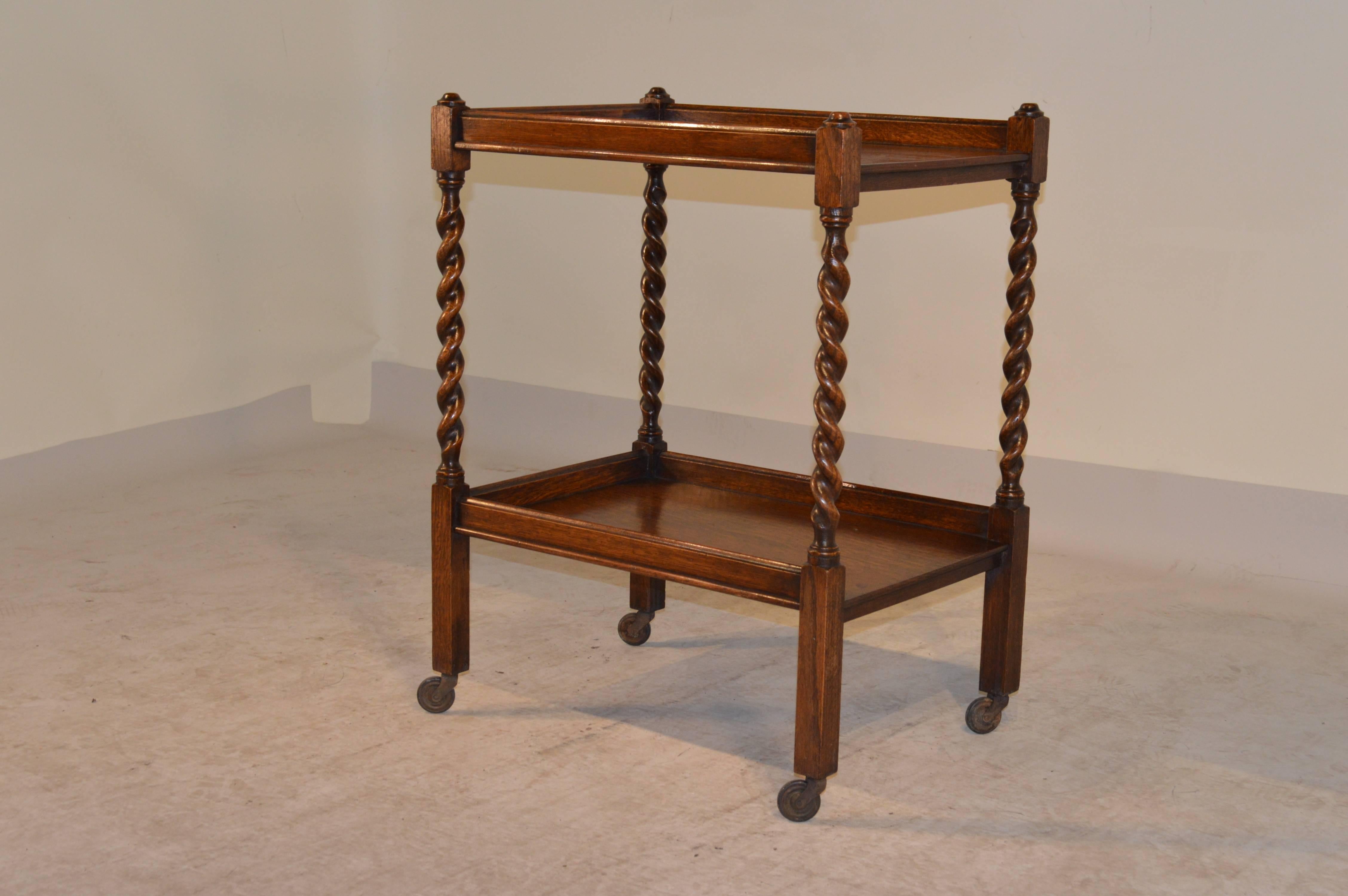 Circa 1900 English oak tea cart with two shelves and hand turned barley twist legs.  Finished with original casters.