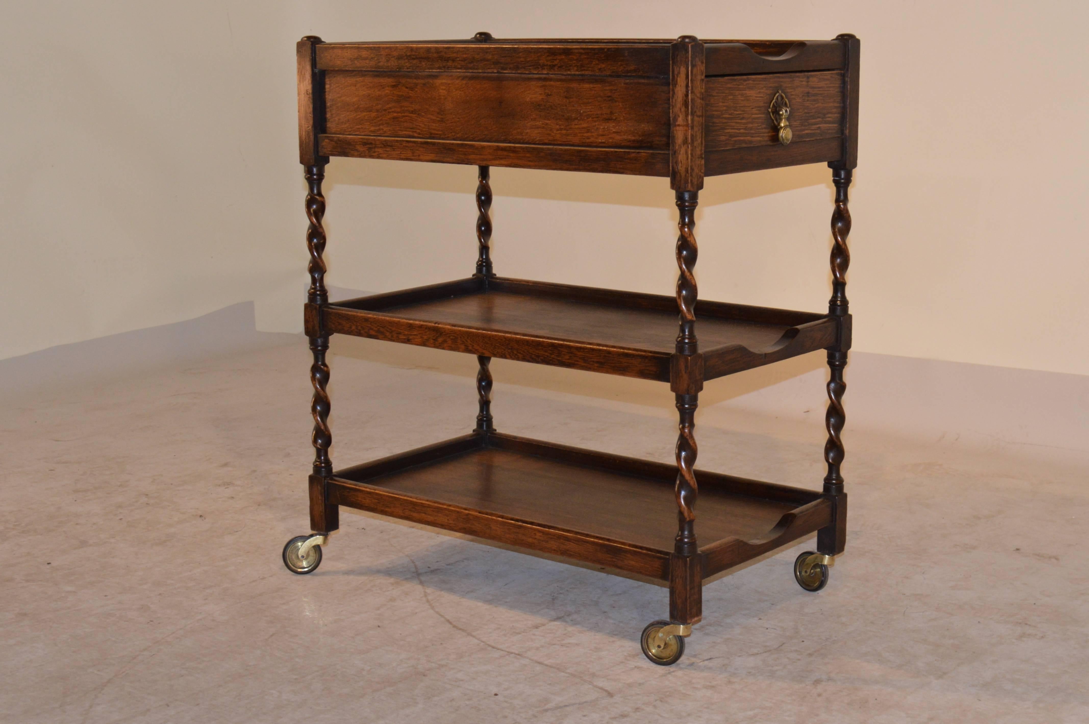 Circa 1900 English oak drinks cart with three shelves and a single drawer.  The legs are hand turned barley twist and the piece is supported on casters.