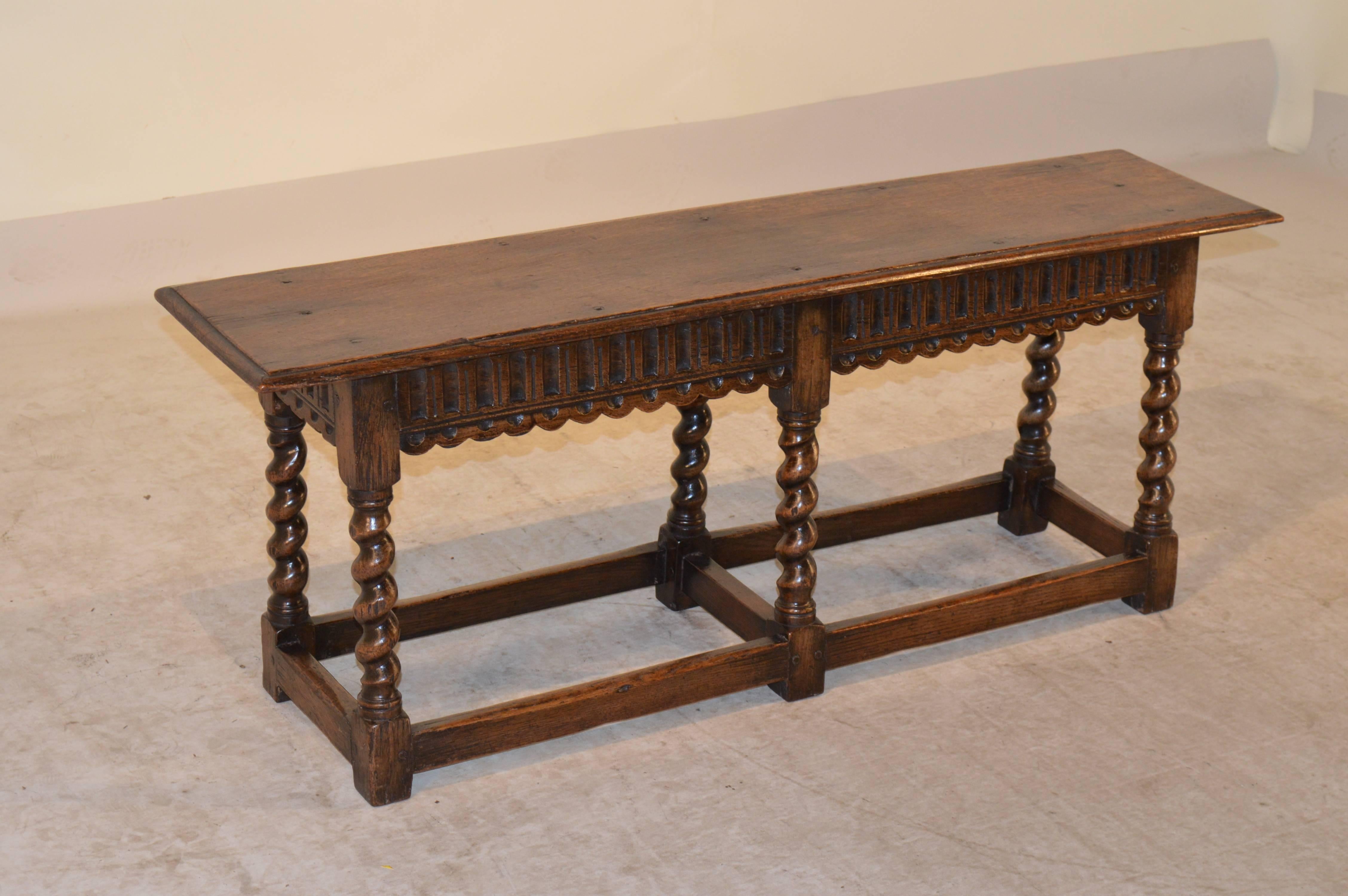 19th Century English oak joint bench with pegged construction.  The top has a beveled edge, following down to a hand carved apron with a scalloped bottom edge and is supported on hand turned barley twist legs, joined by stretchers.