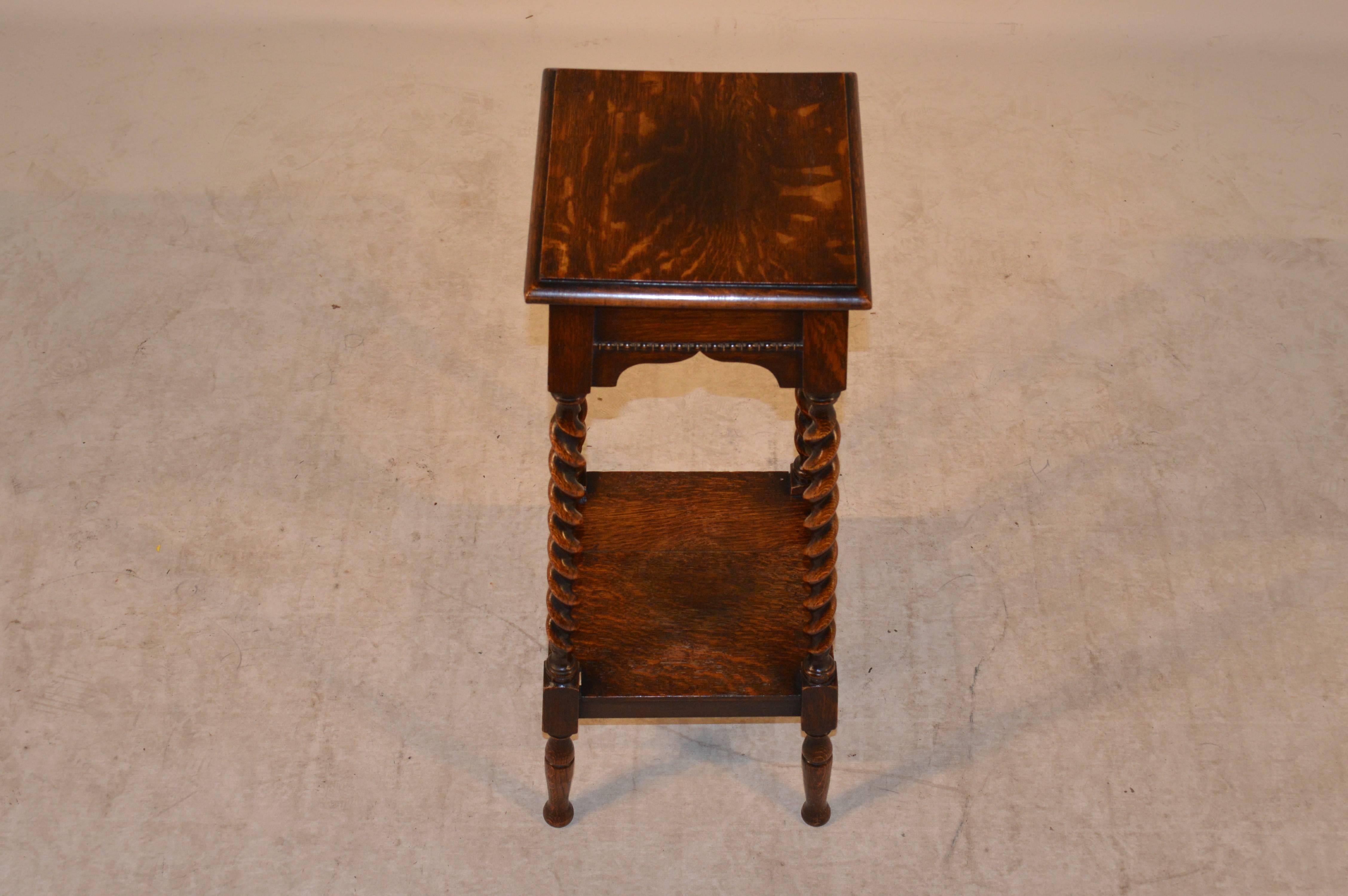 Late 19th century English oak plant stand with two shelves. The top one is beveled around the edge and follows down to a scalloped apron with beading decoration and is supported on barley twist legs, joined by a bottom shelf and raised on turned