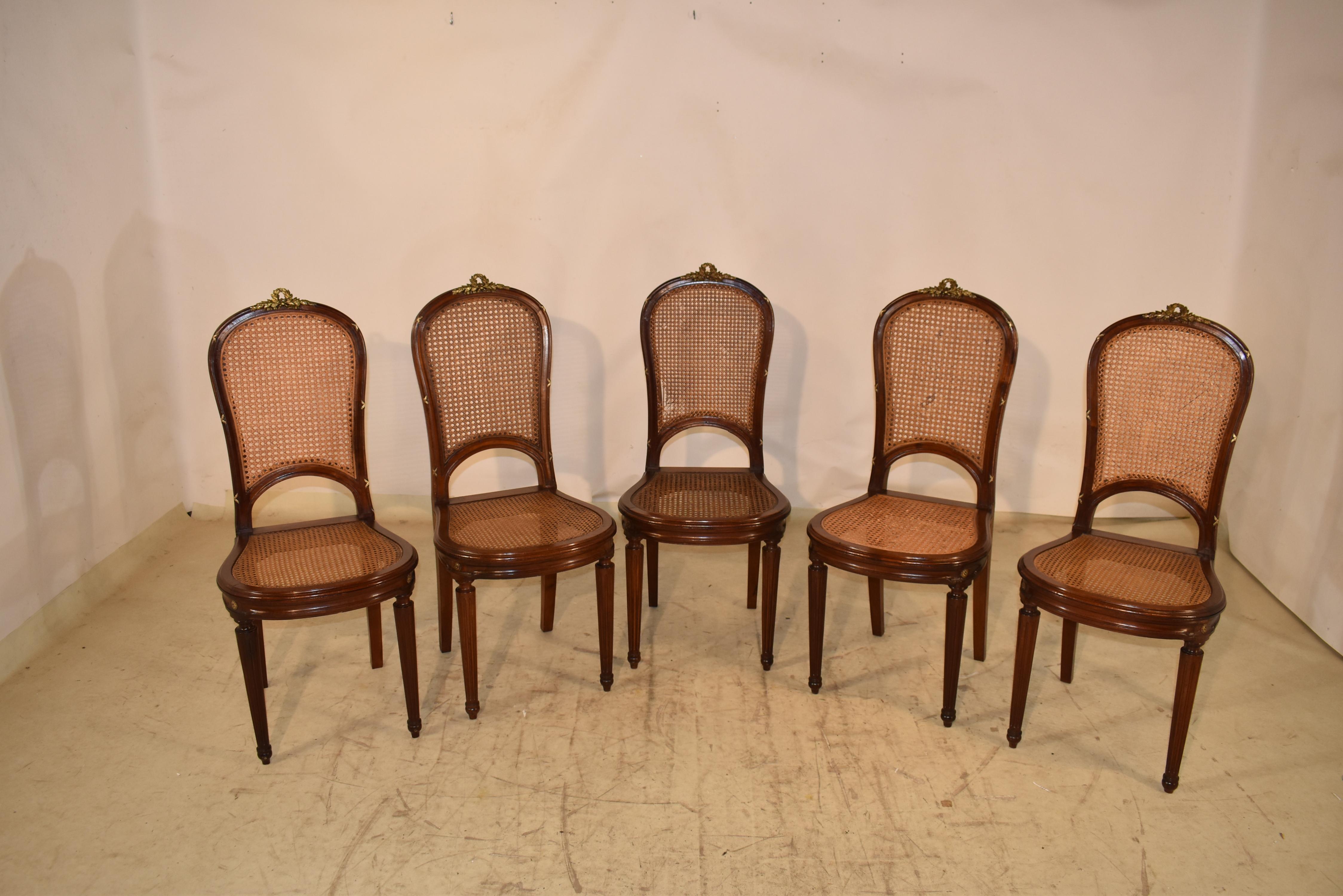 Vers 1900, ensemble de cinq chaises de style Louis XVI en noyer.  Les dossiers incurvés ont des cadres moulés et des accents décoratifs en laiton coulé à la main.  Des couronnes de laurier et des guirlandes se trouvent au sommet et des rubans