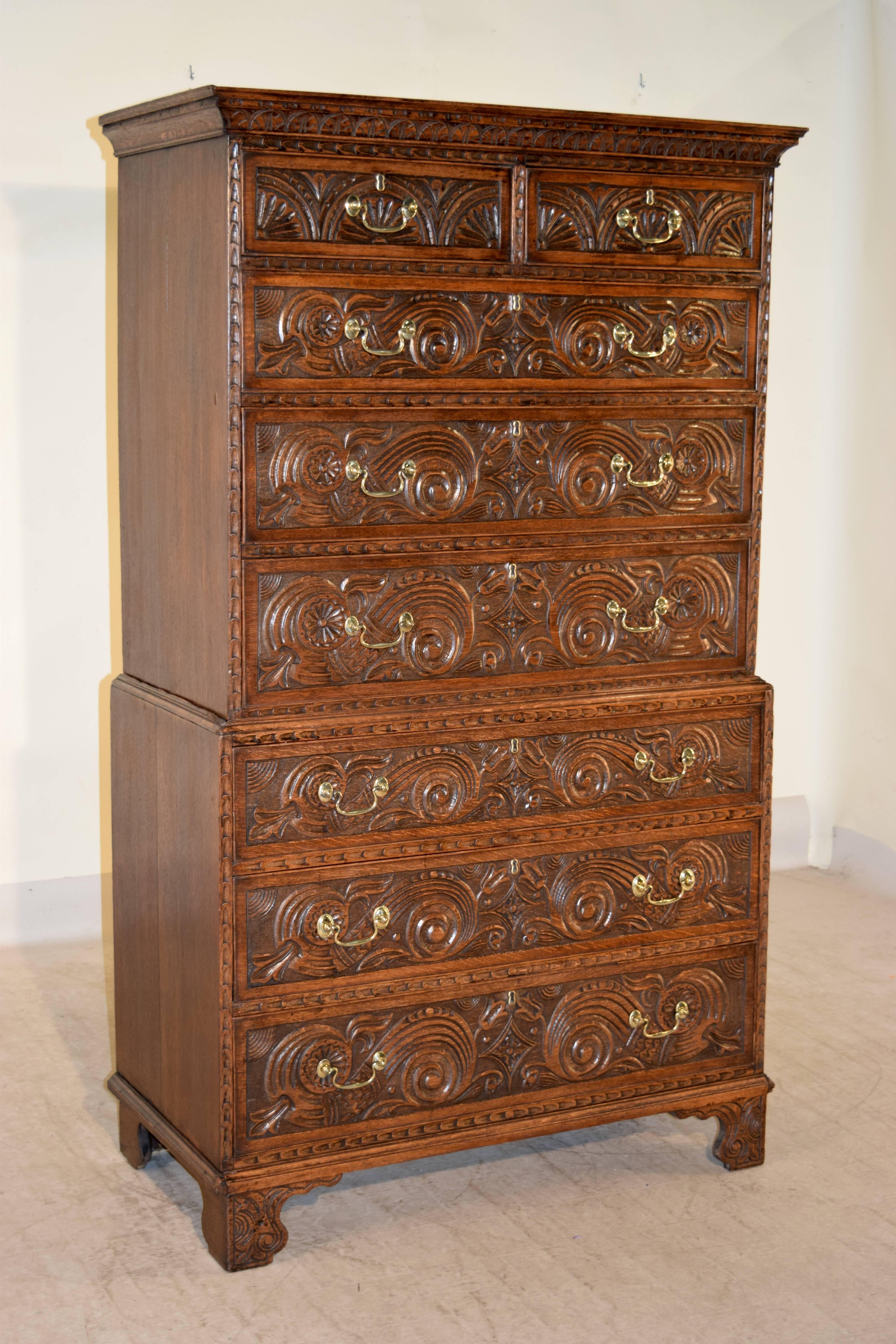 18th century English oak chest on chest with carved decorated crown molding around the top, following down to a two-piece case which has two drawers over six drawers. The sides of the chest are simple and the chest is supported on carved decorated