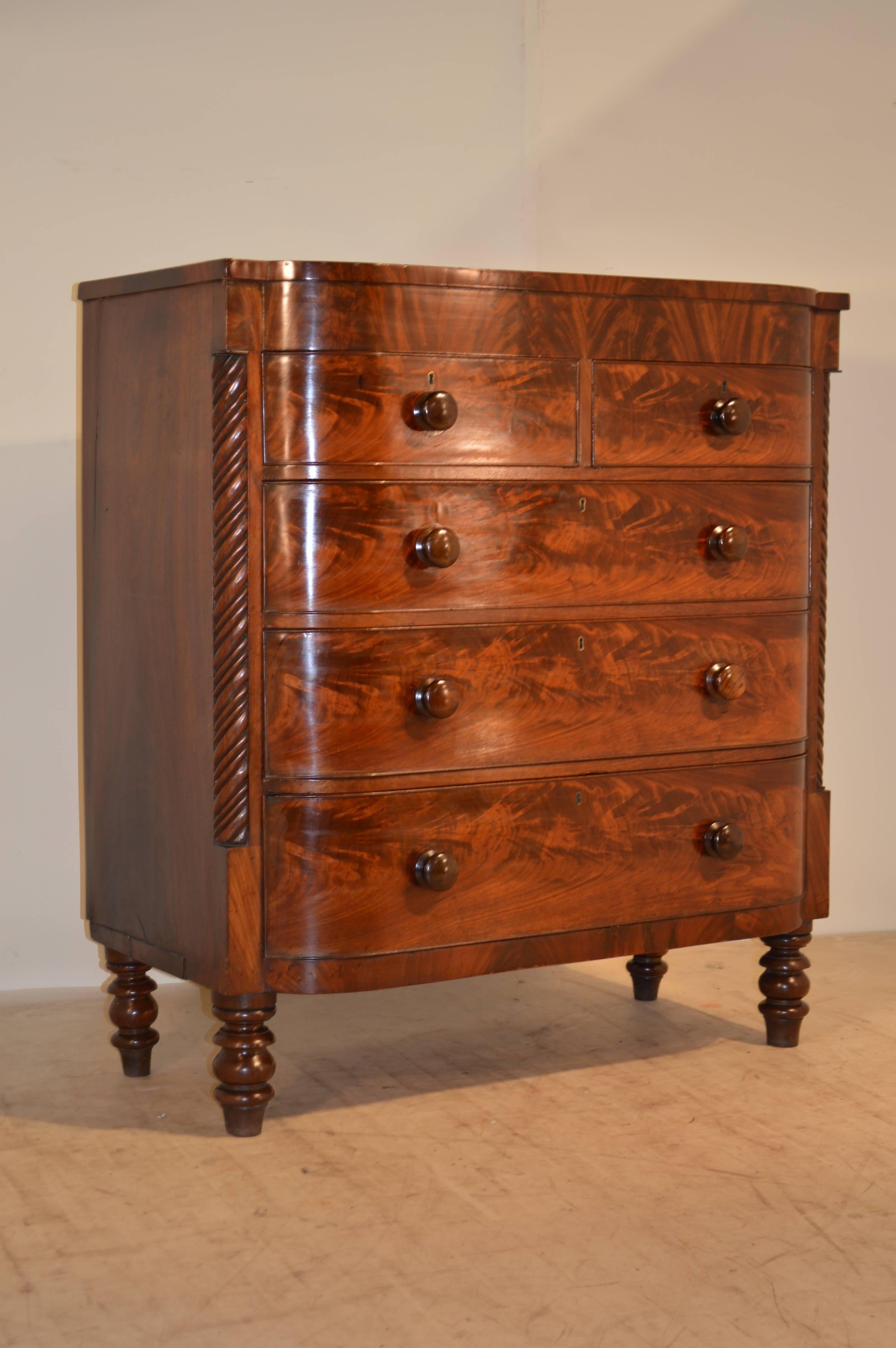 19th century English flame mahogany bow front chest on tall, turned feet. Piece has two small drawers and three larger drawers, flanked by hand-carved twist-design quarter columns. Top has some small veneer repairs around the edges. Age wear,