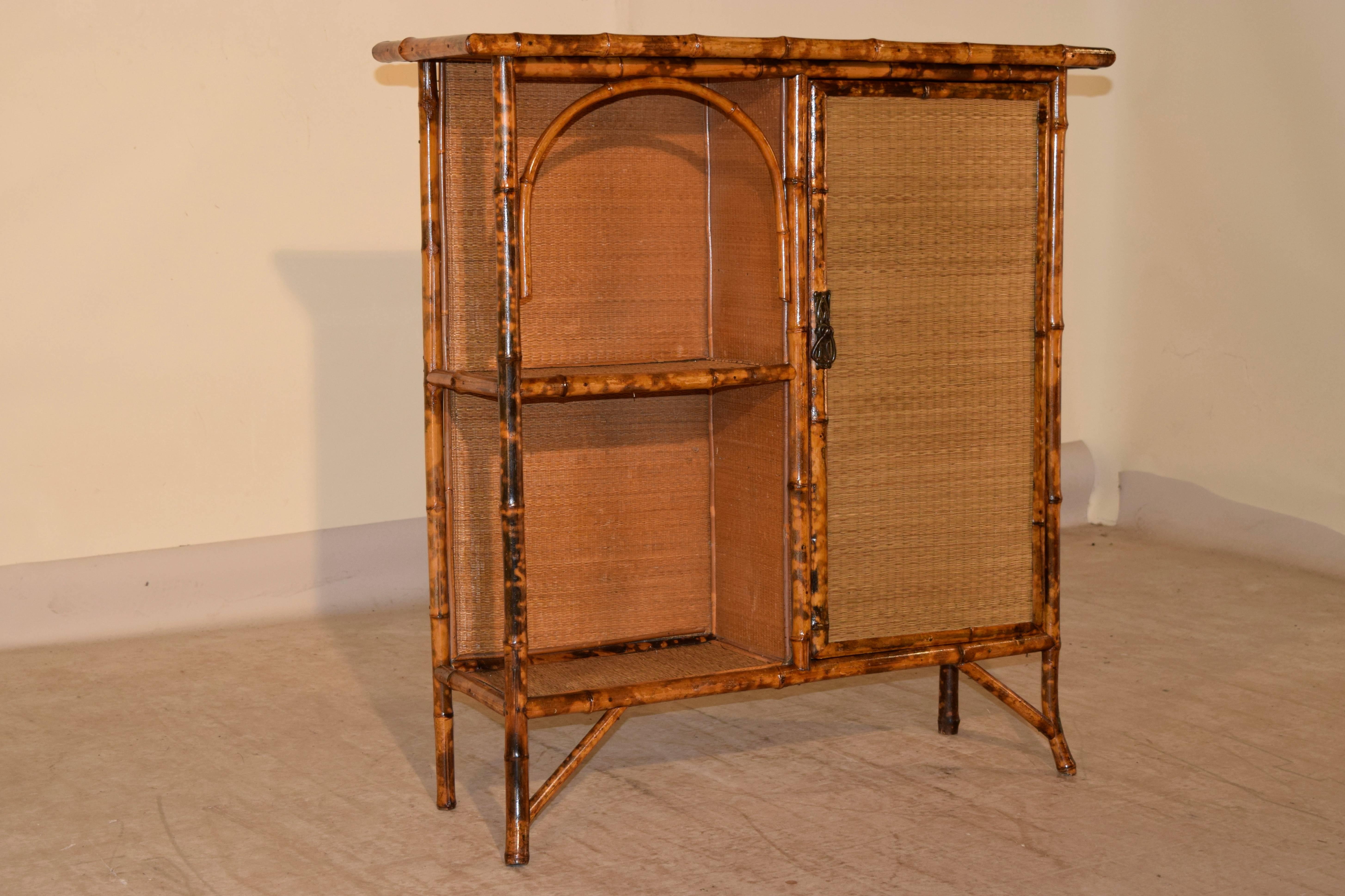 19th century French bookcase made from tortoise bamboo and pine. The top, shelves, and door are covered in rush, and the backing for the bookcase is burlap. There are two open shelves on the left side, and in the cabinet are three more pine shelves