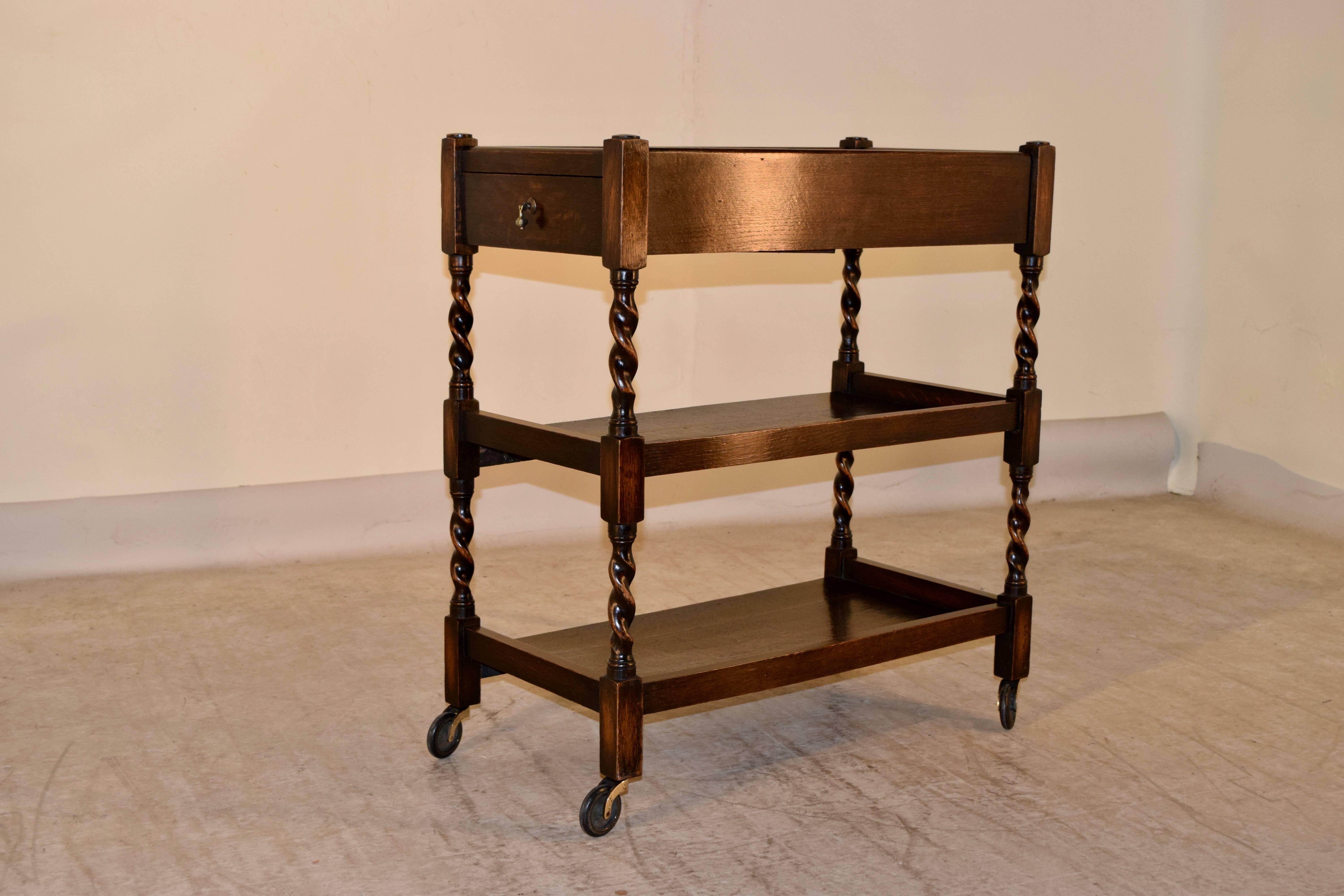 English oak drinks cart with three shelves. The top shelf has a gallery around the top, and a single drawer, following down to two lower shelves, separated by hand-turned barley twist legs. The lower shelves have galleries on three sides, for easy