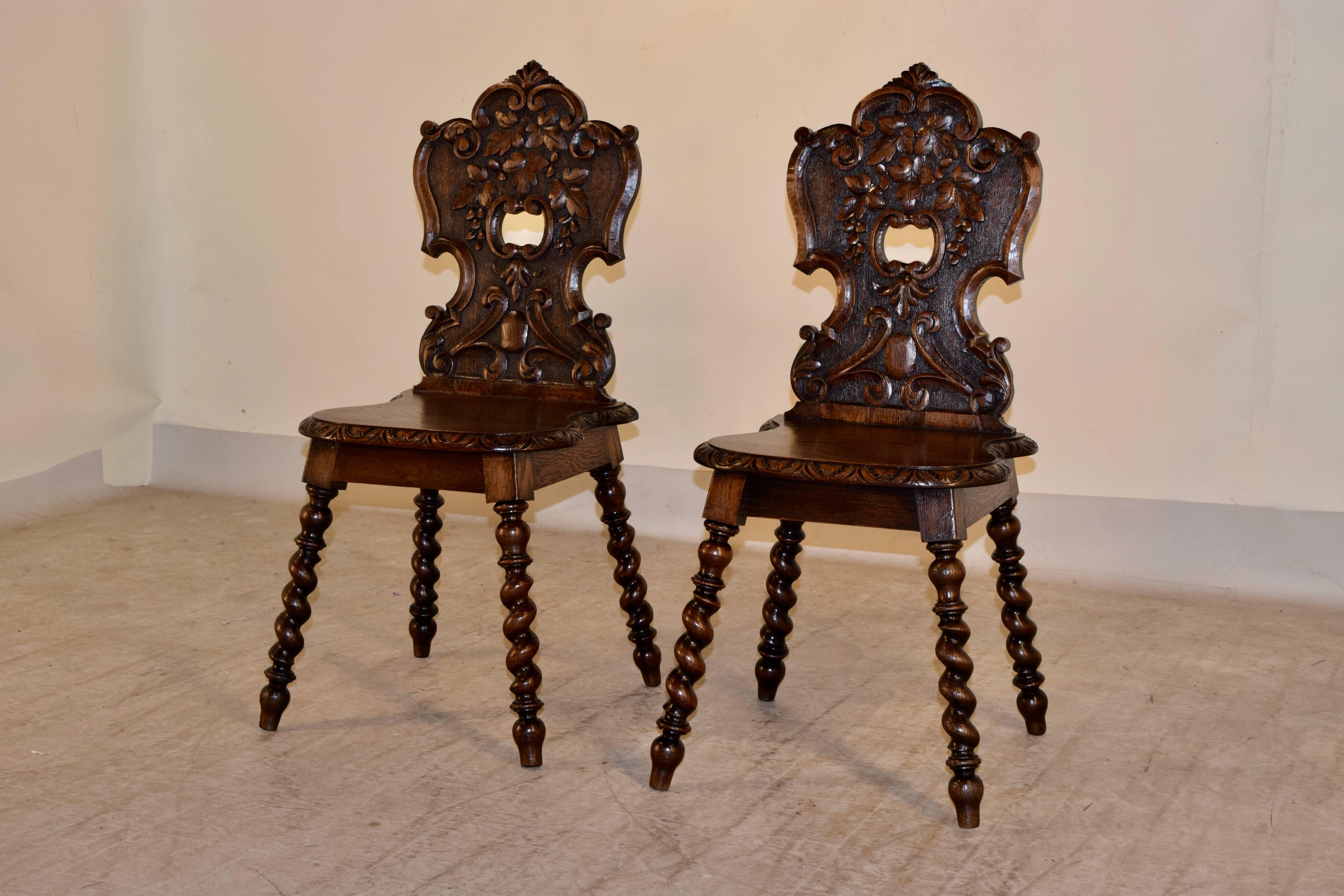 19th century pair of carved oak hall chairs from England. The backs are shield shaped and have a central piercing. They are carved with leaves. The seats have beveled and gadrooned edges, and have simple aprons. They are supported on hand-turned