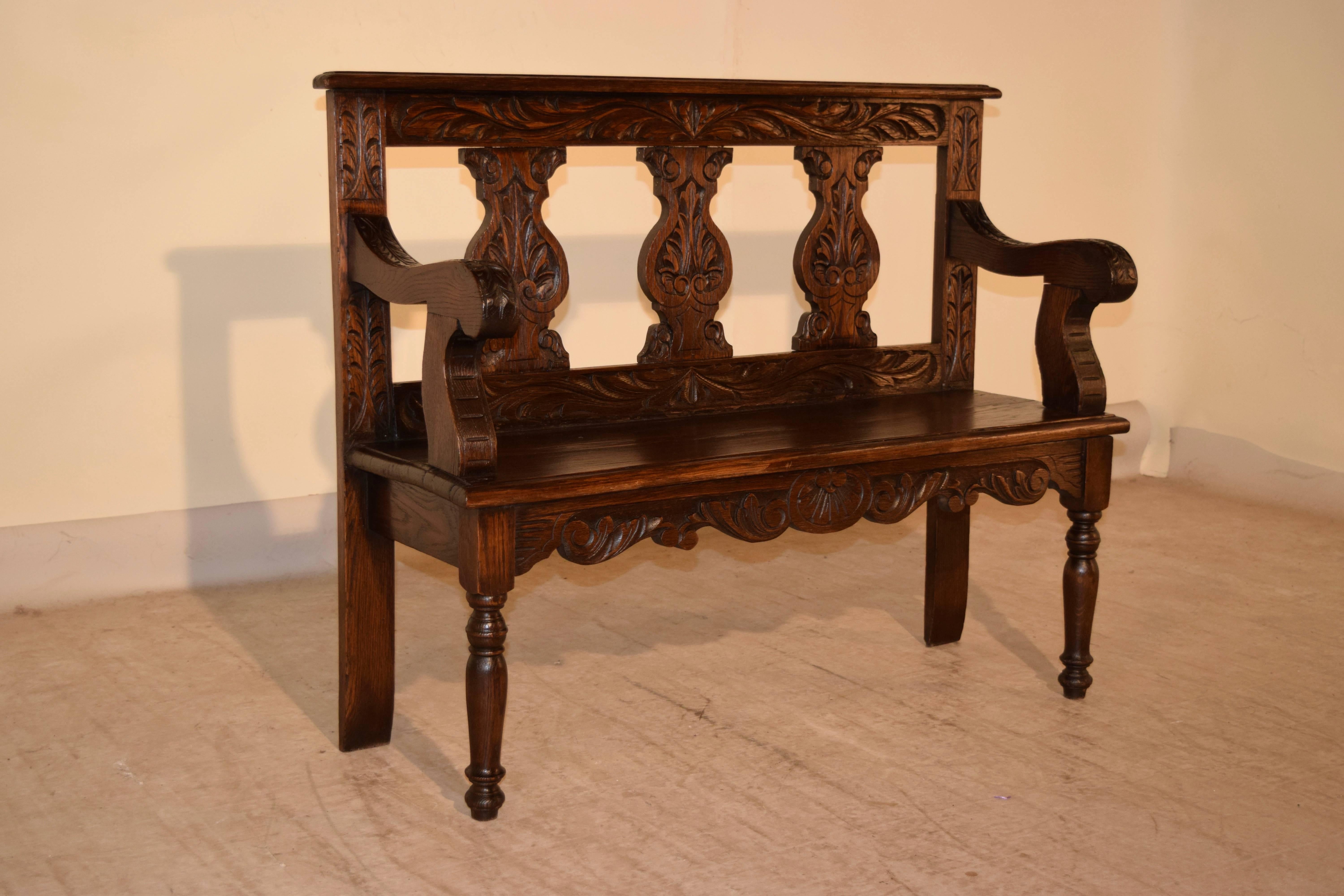 19th century French settee made from oak. The back is carved and has three vase shaped panels, following down to a seat with a bevelled edge along the front, and carved arms. The legs are hand-turned in the front and simple in the back for easy