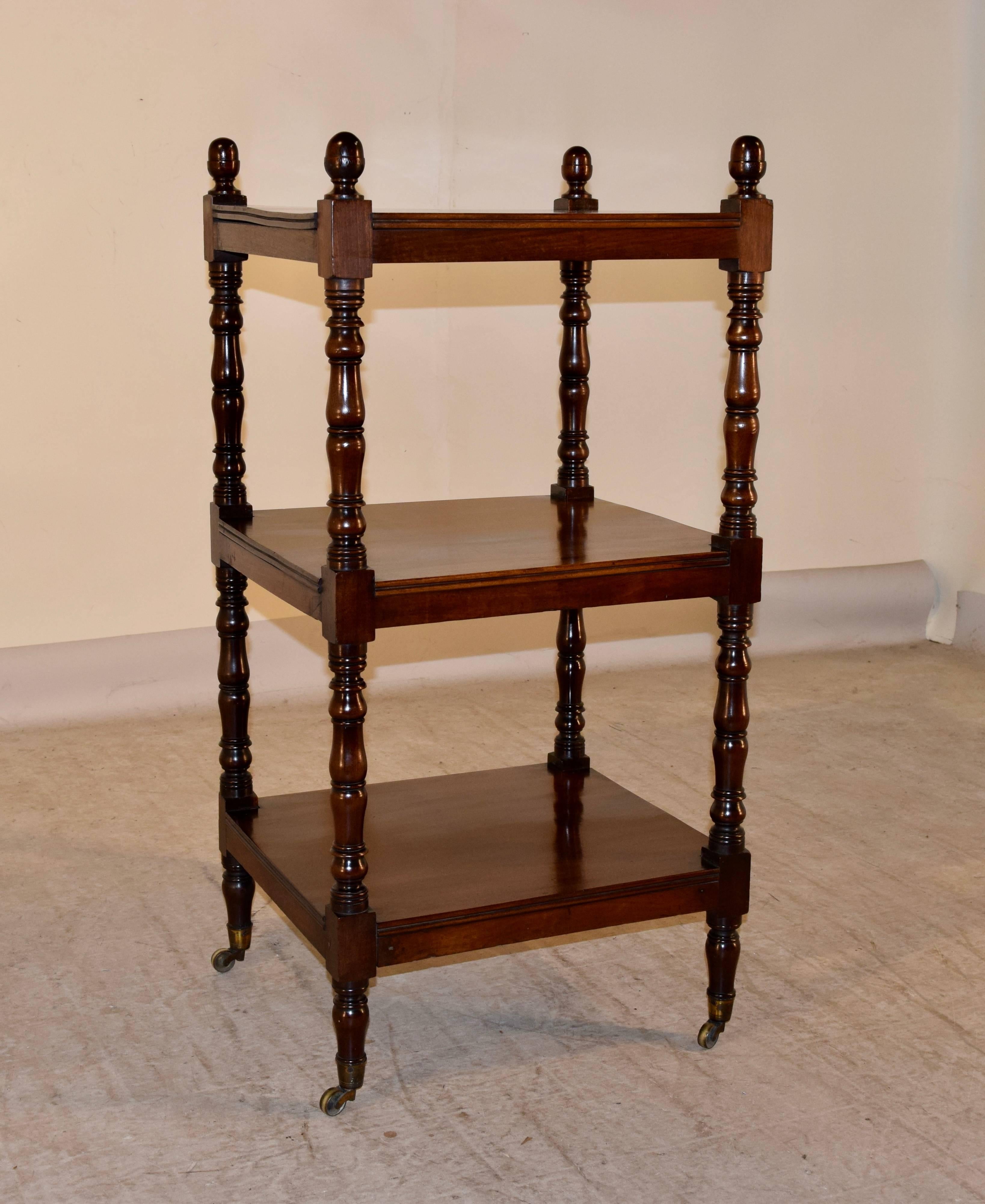 19th century English Mahogany dumbwaiter with lovely turned finials in the shape of acorns. Three shelves with reeded edges separated by hand-turned shelf supports. Resting on original casters.
