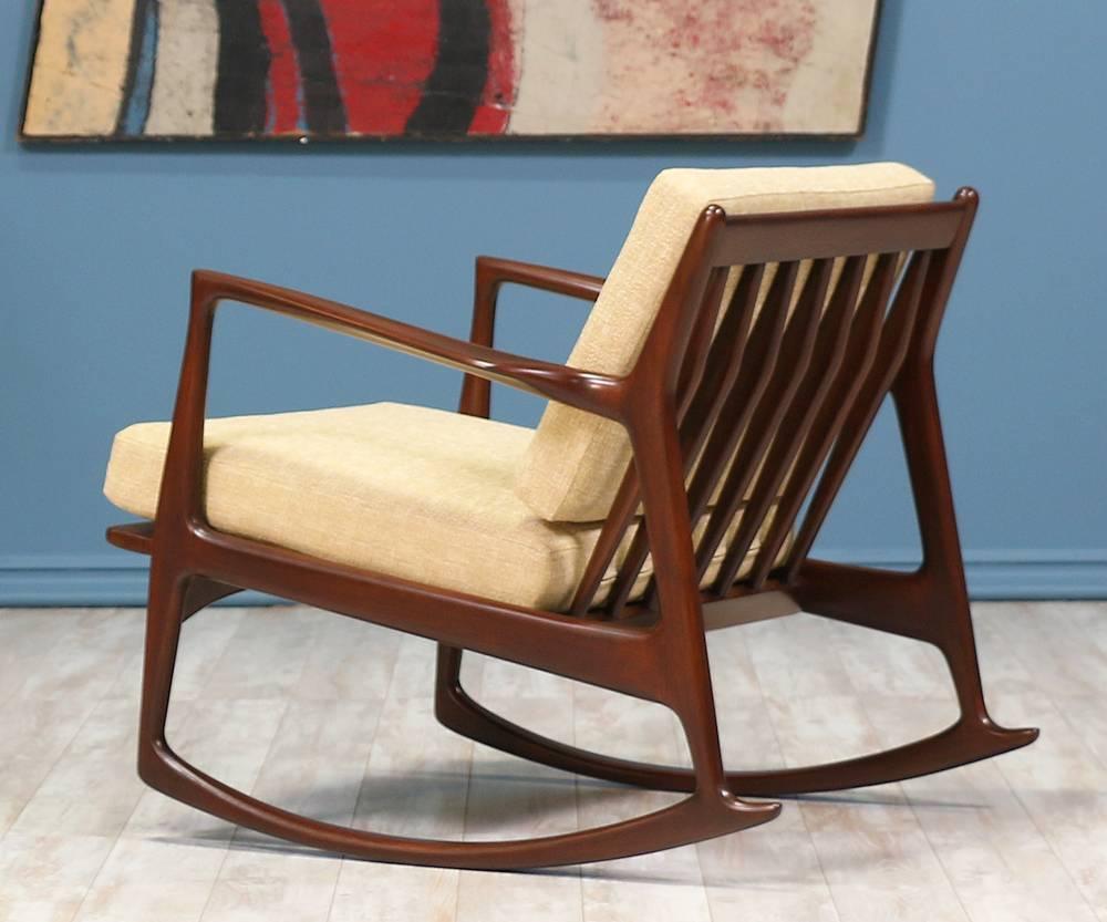 Stunning rocking chair designed by Danish furniture designer Ib-Kofod Larsen for Selig in Denmark c. 1960’s. Featuring a walnut-stained beechwood frame with a slatted back. New high-density foam cushions are newly reupholstered in a creamy tweed