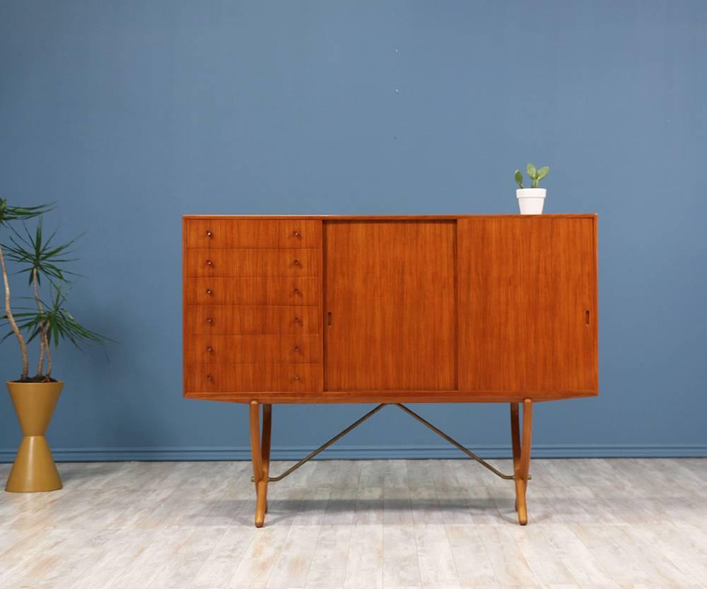 CH-304 Credenza designed by Hans J. Wegner for Carl Hansen and Søn in Denmark in the 1950’s. Teak body is supported by oak “X” shaped legs and accented with brass bars. Features six dovetailed drawers on the left and two sliding doors on the right