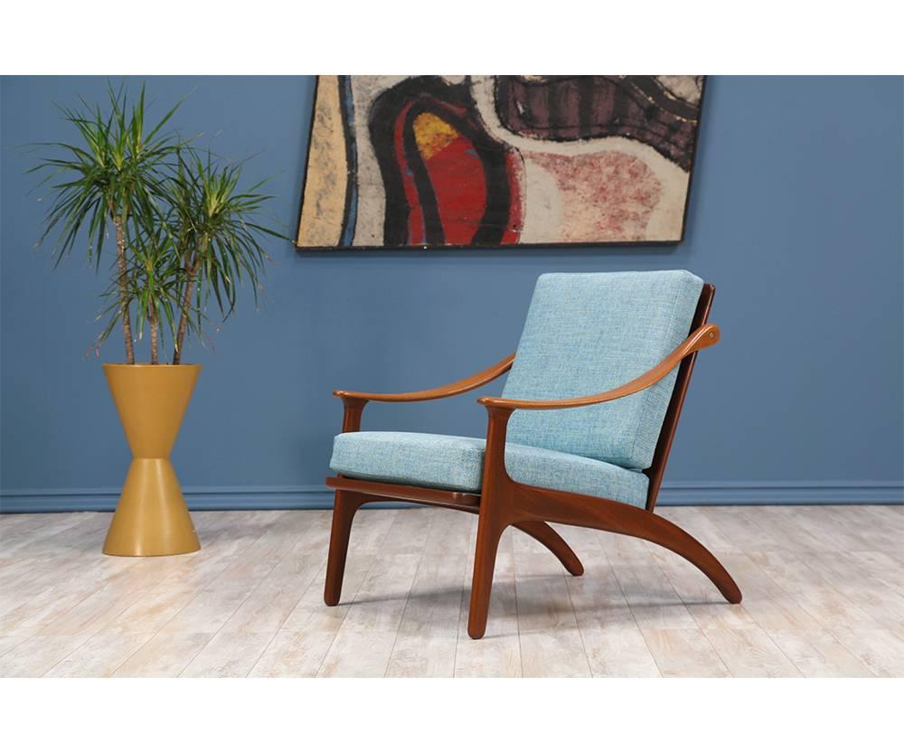 Lounge chair designed by Danish furniture designer, Arne Hovmand-Olsen, for Mogens Kold in Denmark circa 1950’s. Featuring a teak wood frame with five vertical spindles adorning the back, ascending, curvilinear arm rests, and sculptural legs, this
