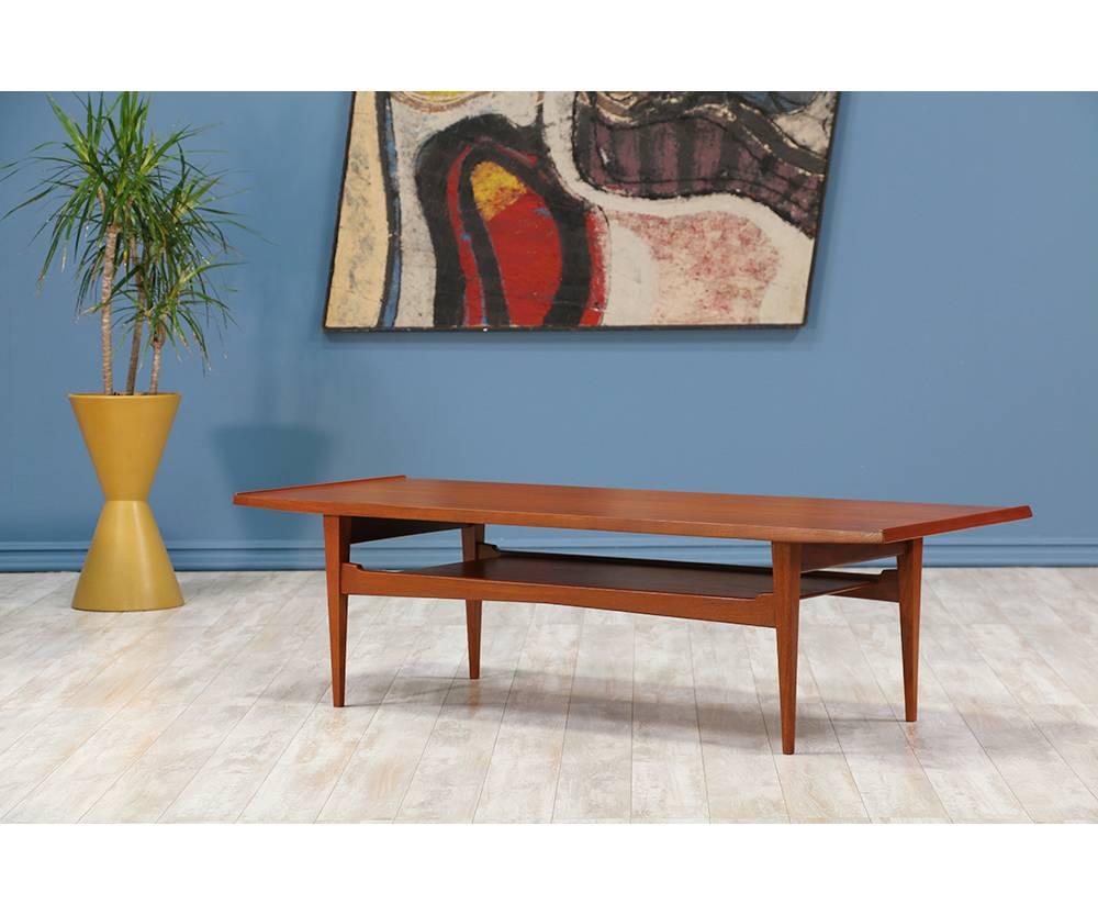 Danish Modern Coffee table manufactured by Moreddi in the United States circa 1950’s. Comprised of a beautiful teak wood, this table features tapered legs, a surface top with raised lip detail along the shorter edges and a secondary tier supported