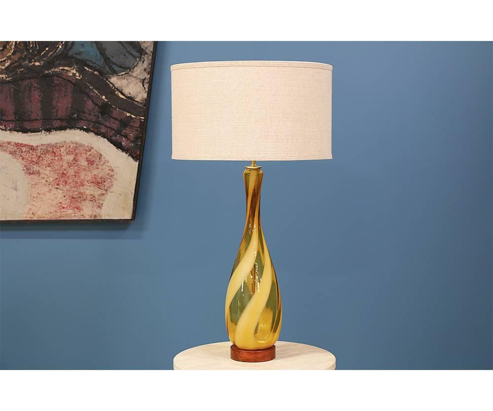 Pair of Mid Century Modern Murano glass table lamps designed and manufactured in the United States in the 1960’s. These lamps feature a swirl design comprised of Murano amber glass that are mounted atop walnut wood bases. New brass hardware and