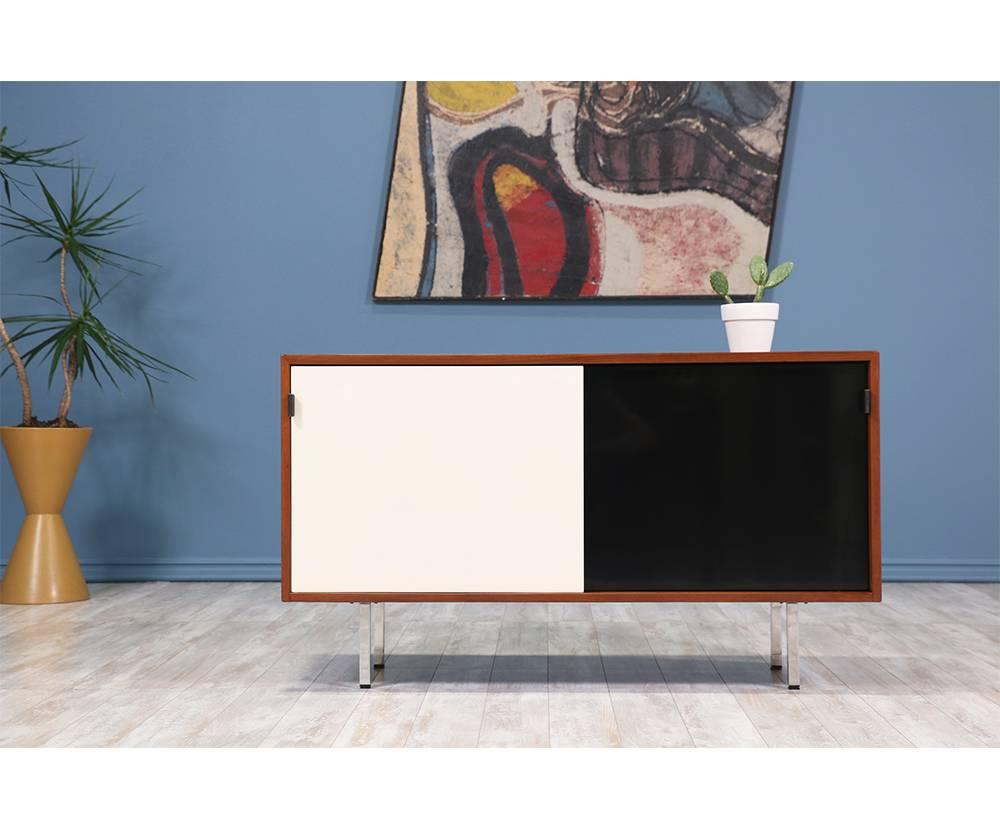 Mid-Century Modern walnut credenza designed by architect and designer Florence Knoll and manufactured by Knoll Associates Inc. circa 1950’s. This compact credenza features two sliding black and white doors with new leather pulls that open to reveal