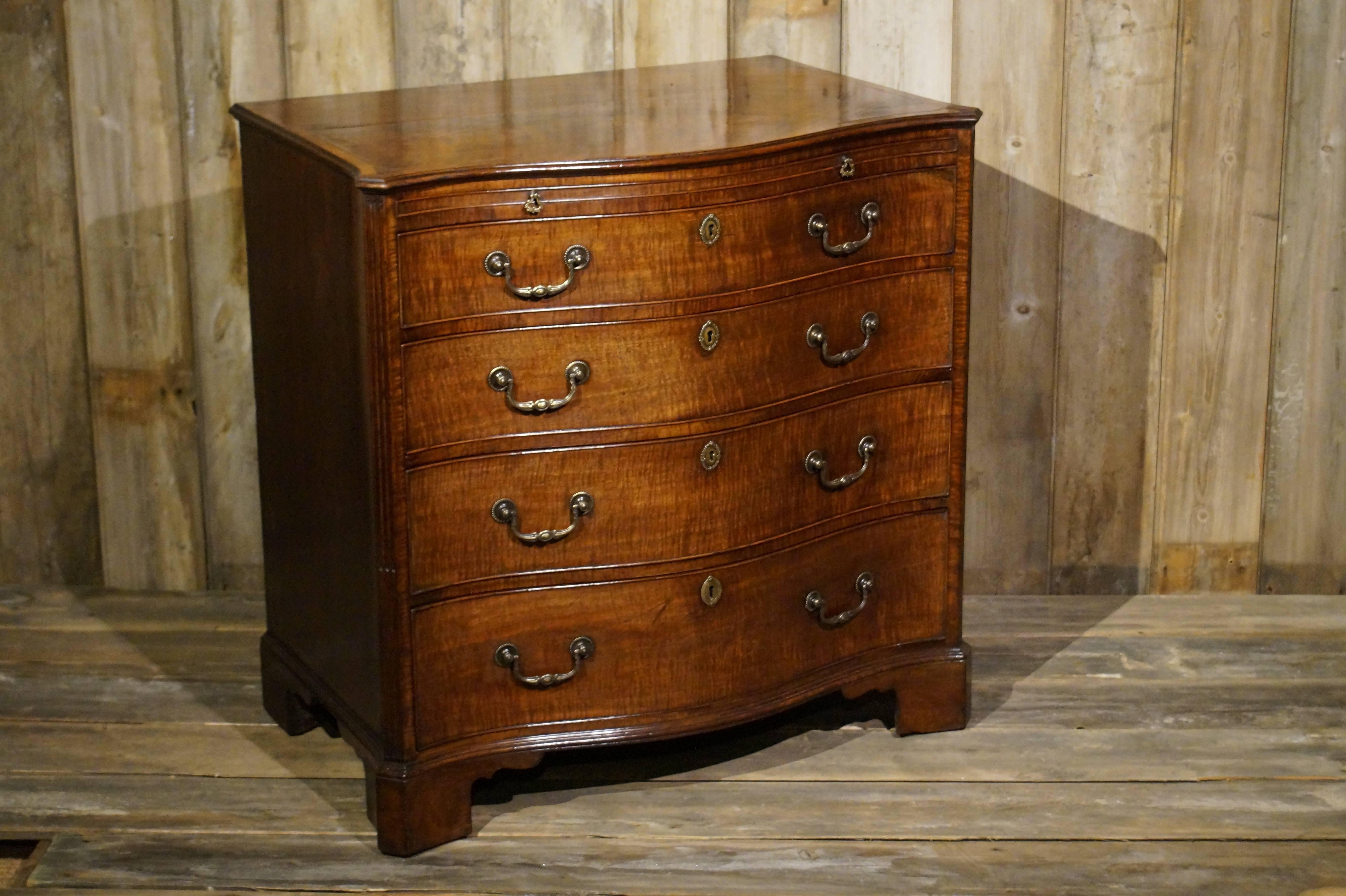 A particularly fine George III period fiddle back mahogany serpentine front chest of drawers. The overhanging cross banded top above a brushing slide and four long graduated drawers flanked by stop fluted canted corners; standing on bracket feet.