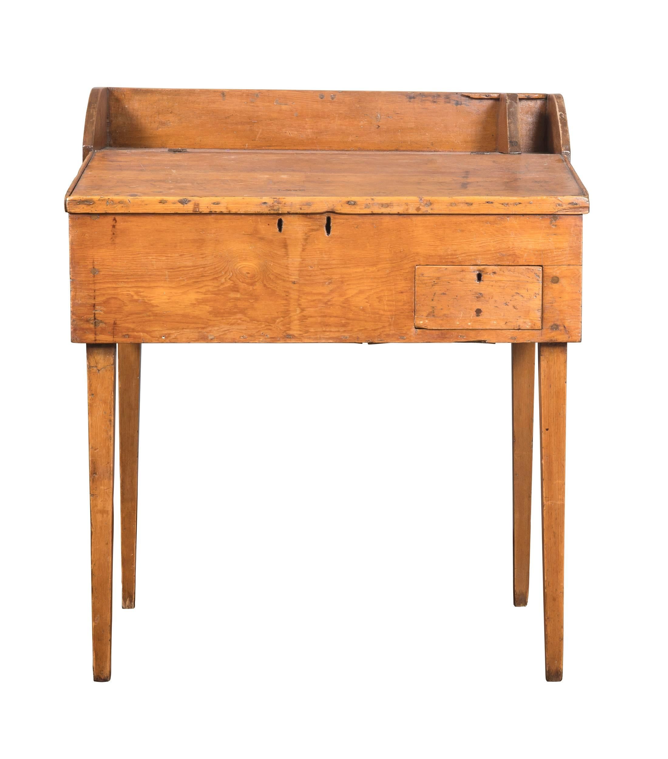 19th century primitive Americana pine desk. Slightly slant top opens to storage below with cubby slots. There are also slots to hold notes and pencils above the desk area and a small drawer below. Pine wood is wonderfully patinated and aged over the