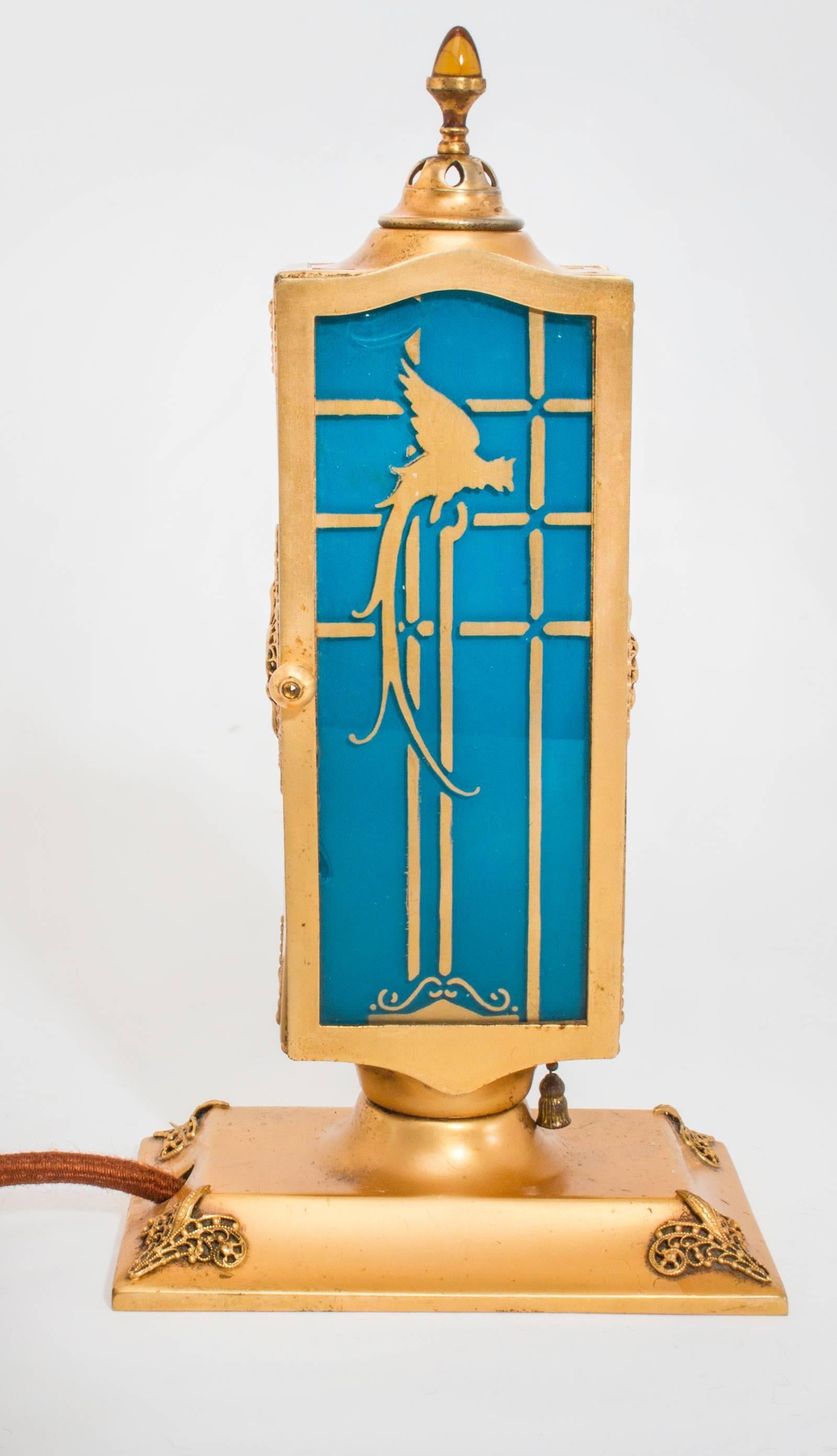 DeVilbiss perfume lamp from 1926. Two blue glass doors with gilt parrots on each doors. Interior of the glass doors are enameled in blue, the front side is parrots in gilt.
The amber glass jewels are set into the door handles and a larger one is