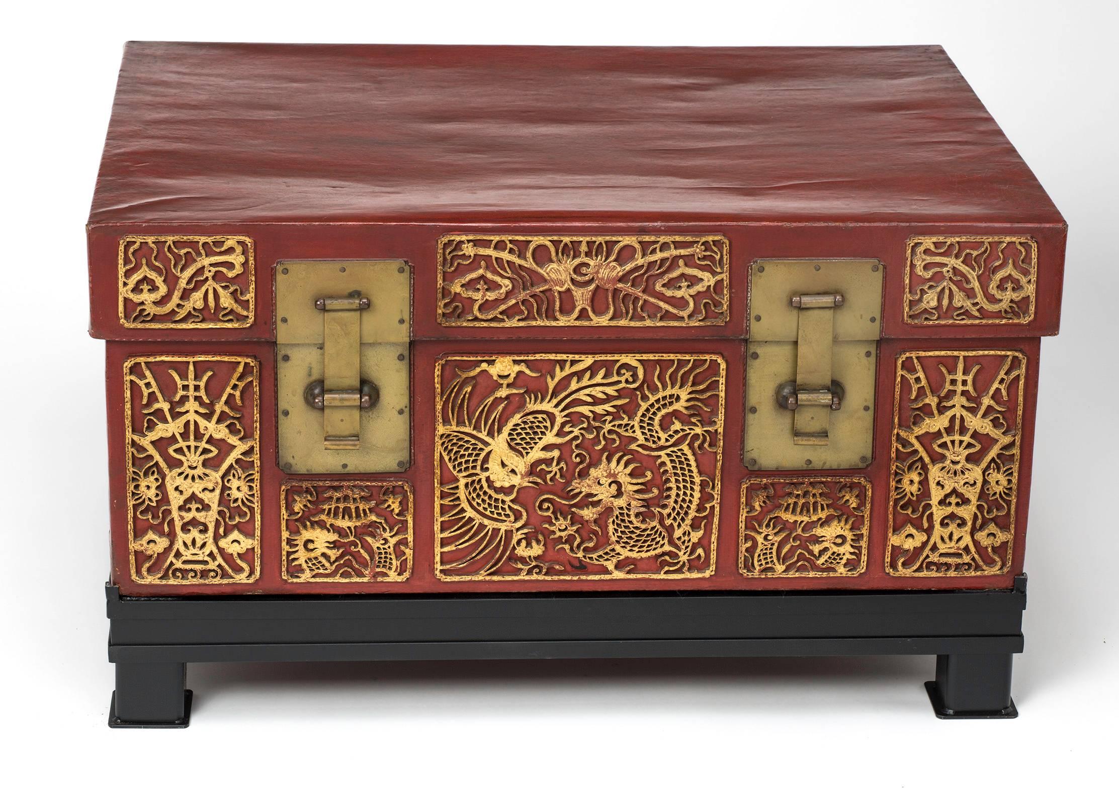 Highly decorative Chinese red leather trunk with carved leather gilt overlay.  Circa 1930s.
It sits on a custom-made iron base. With glass top, it can be useful  as a coffee table or side table.  Glass top is not shown, but included if desired.
