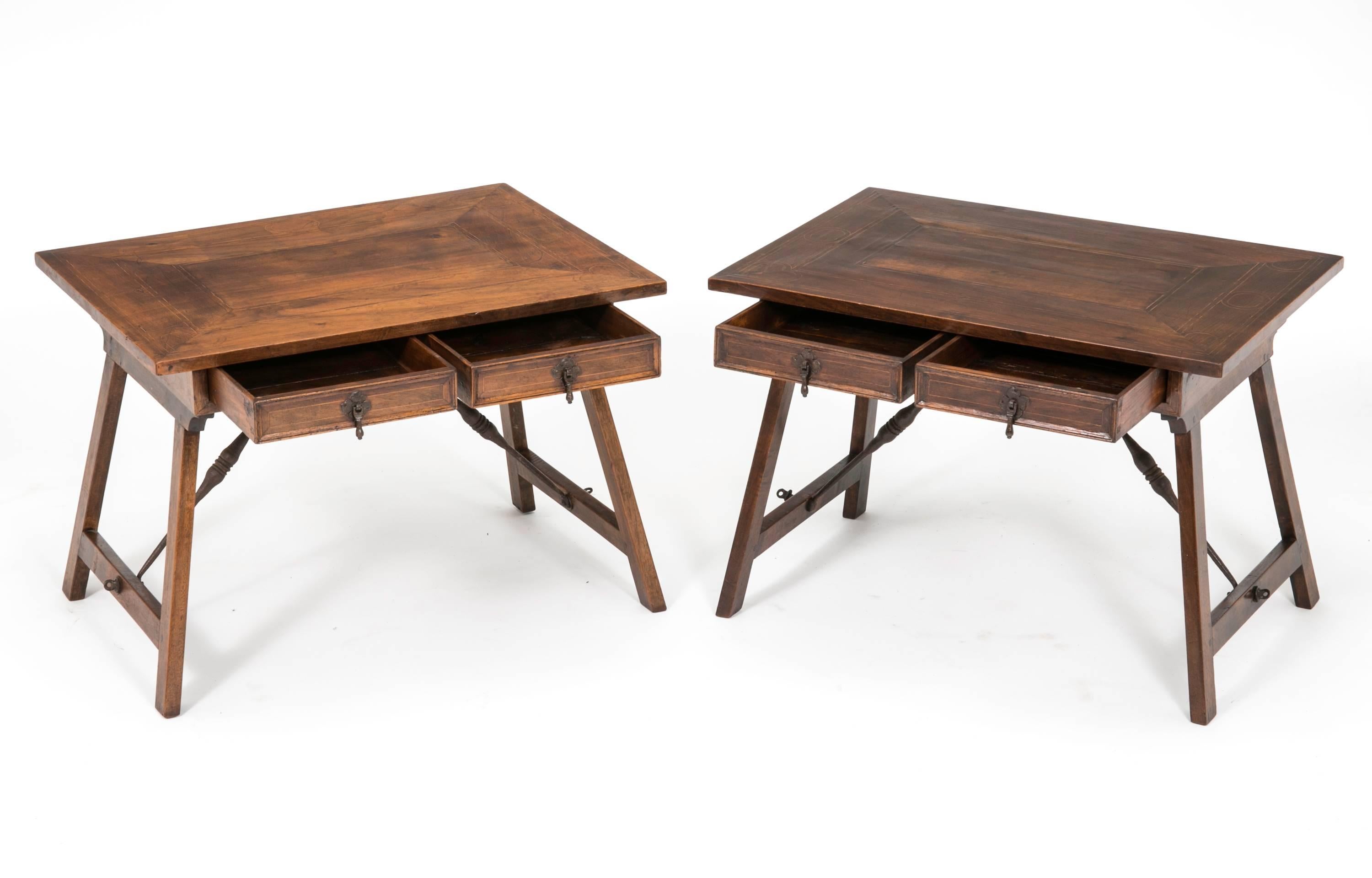 From early 1900s, pair of charming English walnut wood side tables. Each table has two small drawers, supported by iron stretchers. The stretchers are hinged so that the legs will fold down for storage or moving. Great as side tables or cocktail