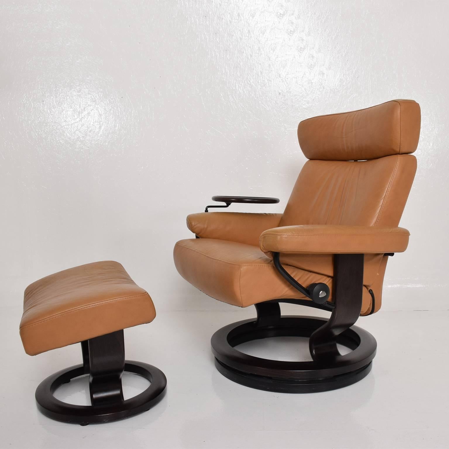 An Ekornes Stressless recliner with matching ottoman and service tray table. 
Camel color leather in very good condition. Dark wood base and round service table. 
Very comfortable ergonomic design. Made in Norway circa 2000
Two chairs are available,