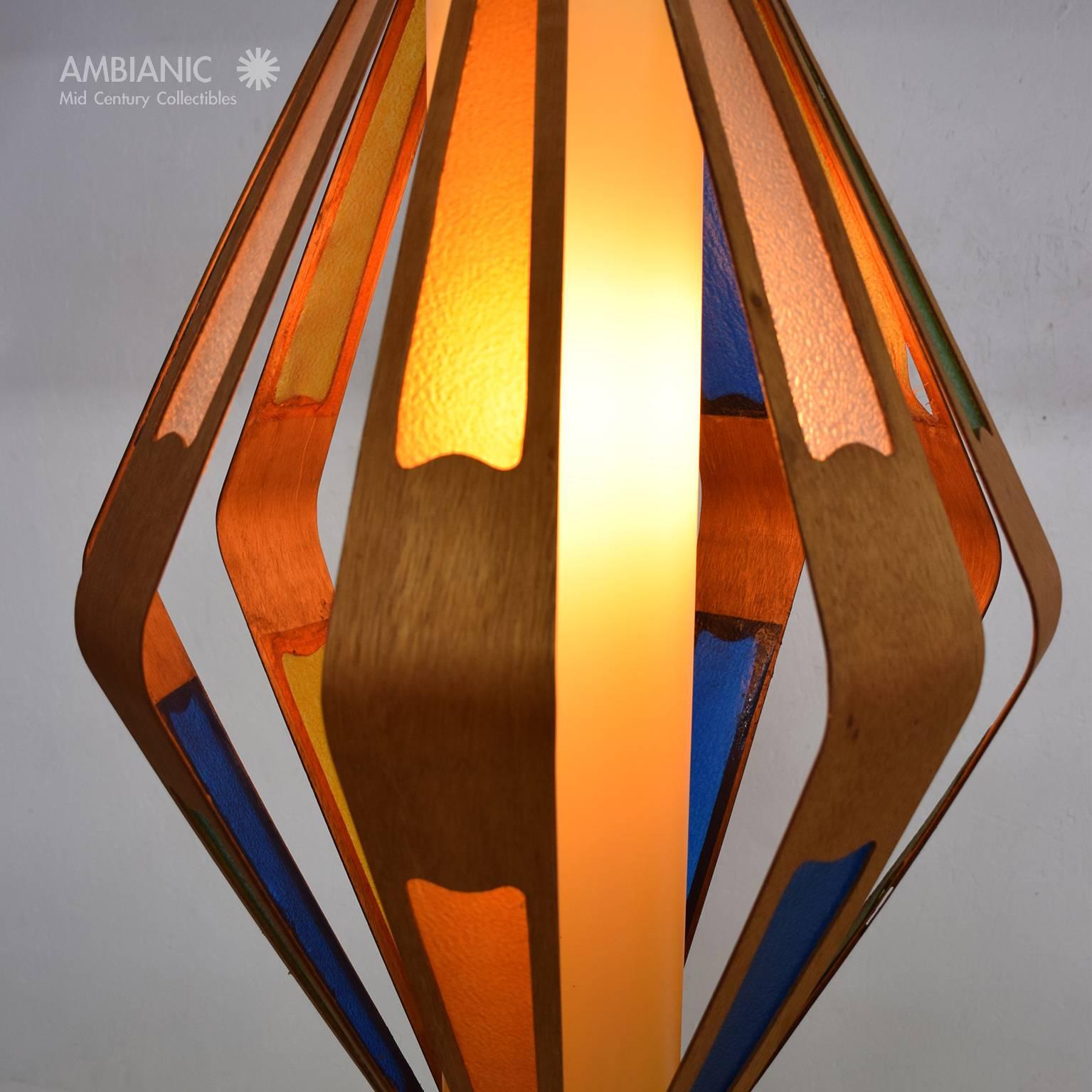 For your consideration a Mid-Century hanging lamp constructed with bent plywood teak and colored plastic inserts. The teak strips are attached into a tubular plastic tube which has been yellowed though out the time.

The wood has small repairs