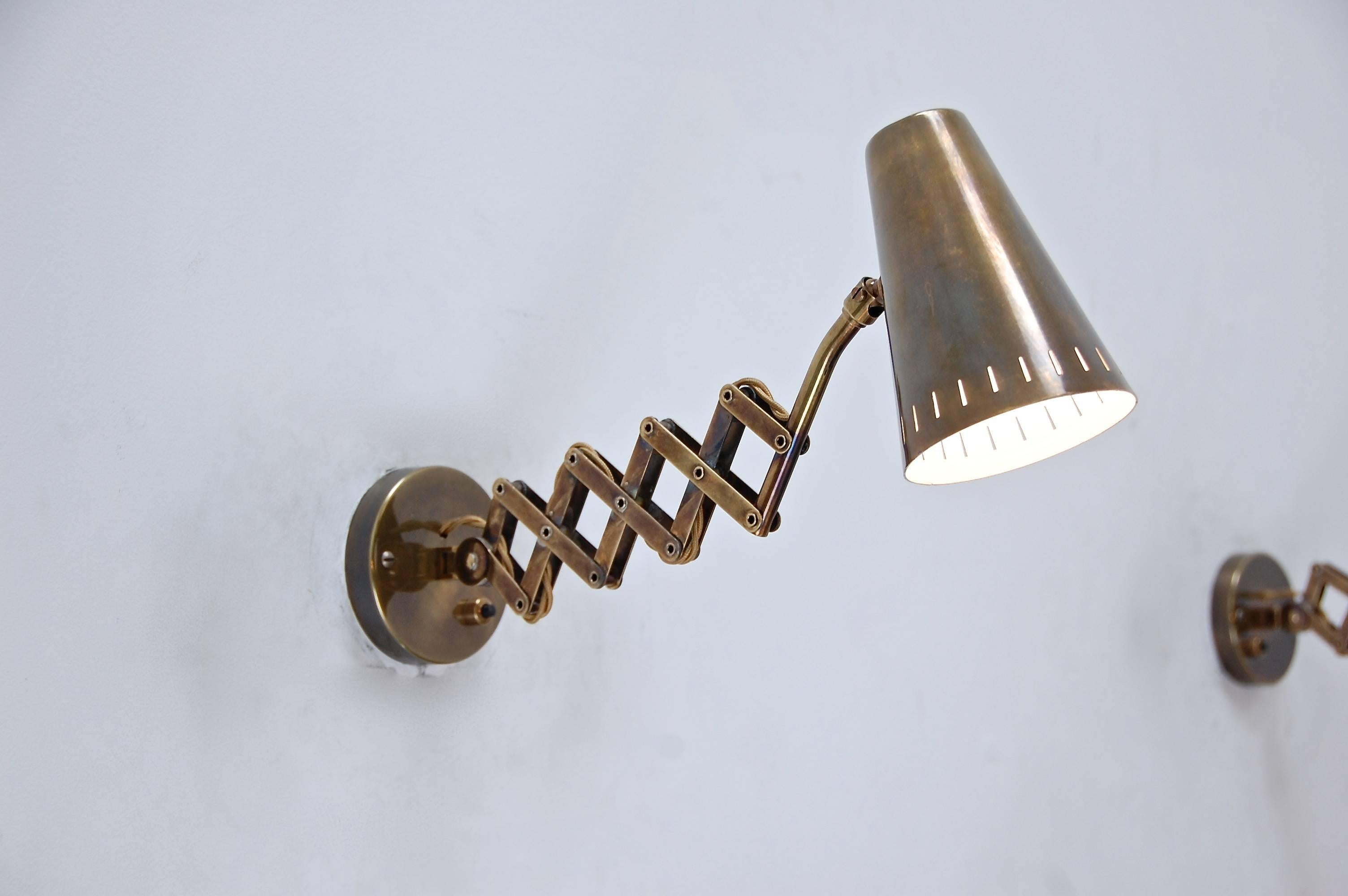 2 wonderful brass scissor sconces from Germany with back plates with a push switch. They articulated in all directions. Patinated brass.
Height: 7”.
Max depth: 19”.
Min depth: 9.5”. 
Width: 4”.
Shade: 4 x 5.5”.
 