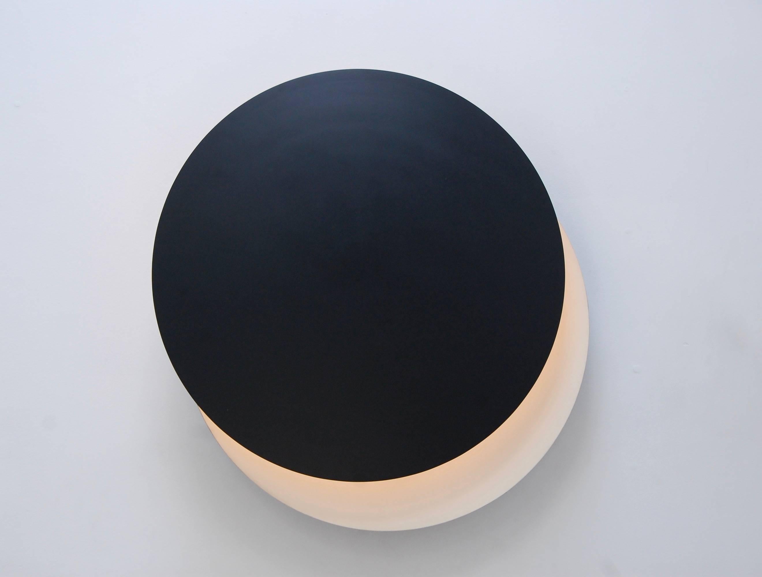 Stunning and dramatic large Luclipse wall fixture. This fixture acts as a mood piece and emits indirect lighting. The eclipse effect is created by a contrast between the front and back shade. The front shade can articulate in any direction to direct