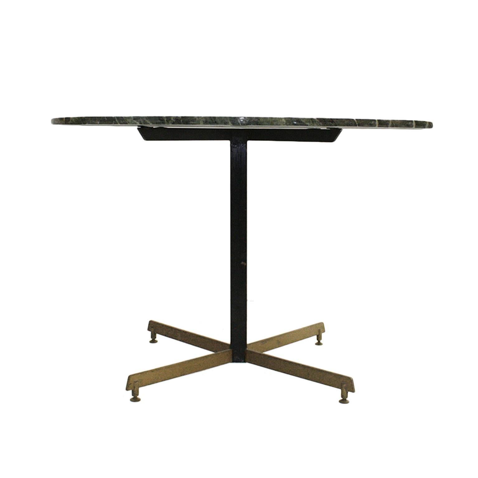 Italian pedestal table from the 1950s with structure made of black lacquered iron and brass foot with blade shape and pivoting pads. Circular envelope of green marble.
 