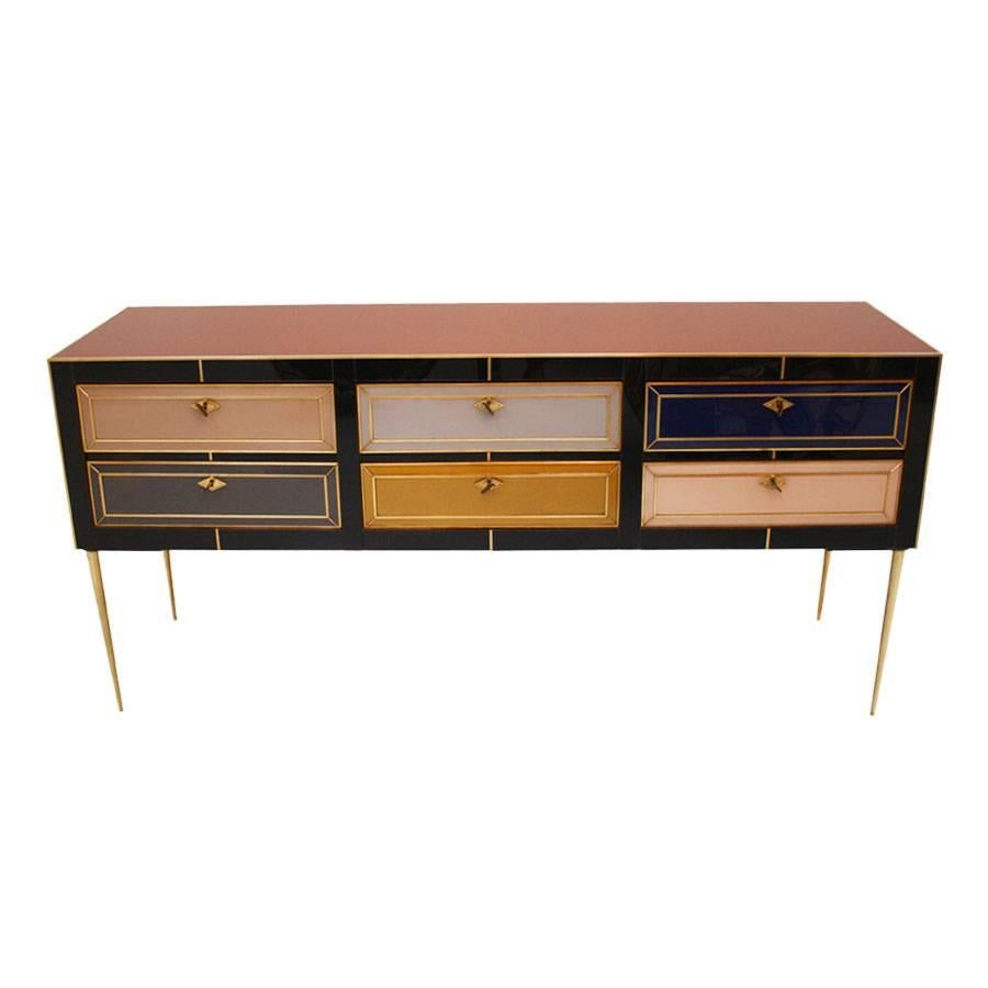 Italian sideboard composed by six drawers with wooden structure covered in colored glass and brass profiles, handles and feet.
